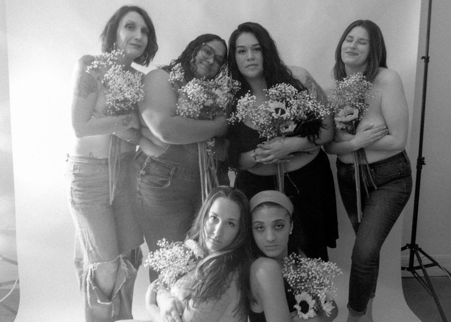 Black and white photo of six women posing together holding baby's breath flowers in a photography studio.