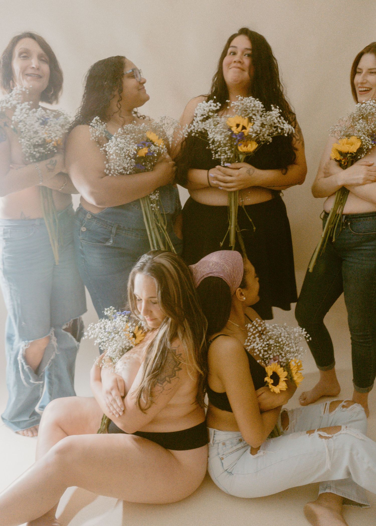 Group of women holding sunflowers and baby's breath bouquets posing together in a casual body-positive photo shoot.