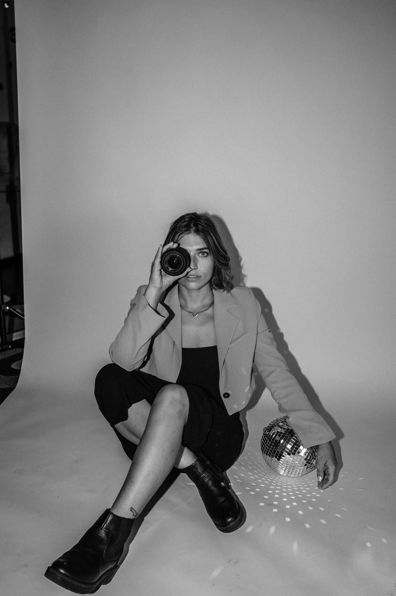Black and white photo of a woman holding a camera to her eye beside a disco ball.