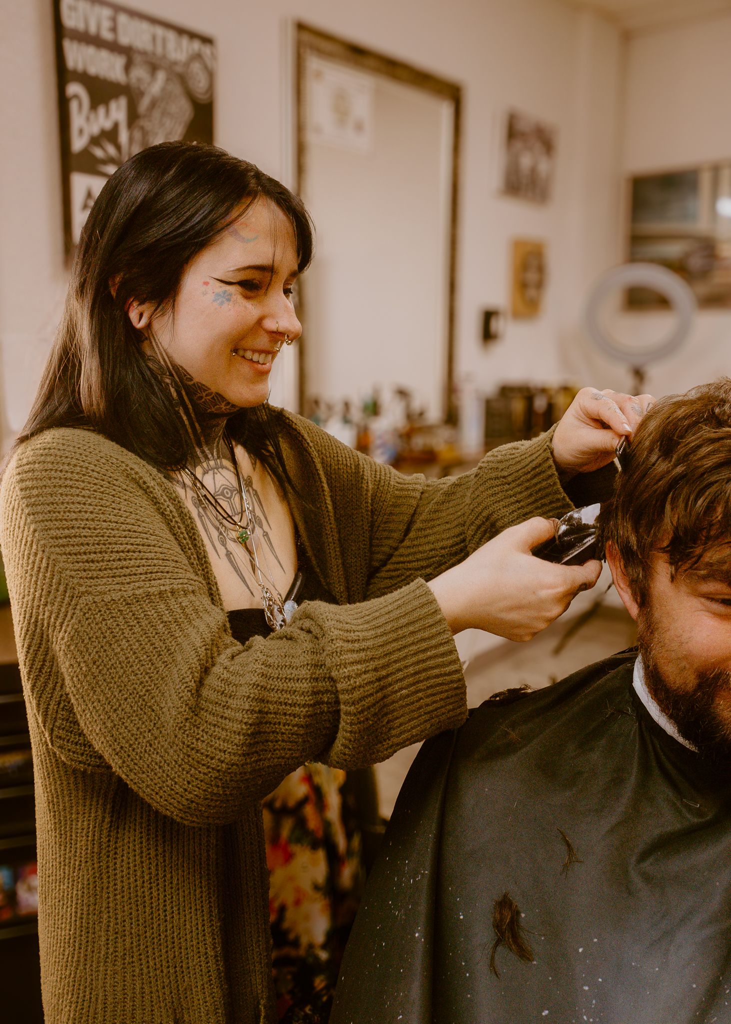 A smiling female barber uses clippers to cut a man's hair in a vintage-style barbershop.