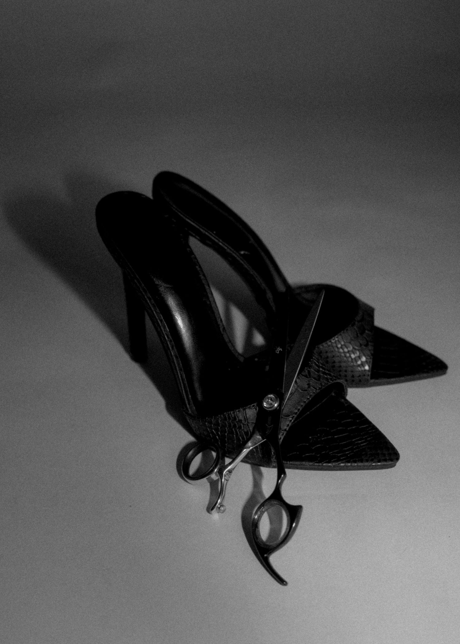 Black leather pointed-toe mule heels with scissors detail, photographed in monochrome on a gray background.