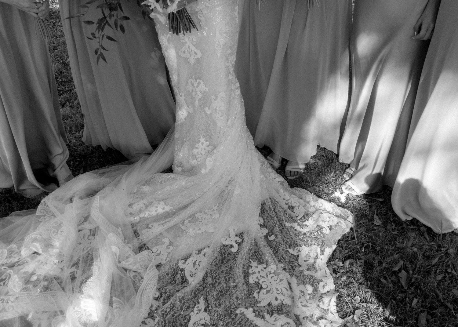 Black and white photo of an elegant lace wedding dress with a long train displayed among bridesmaid dresses.