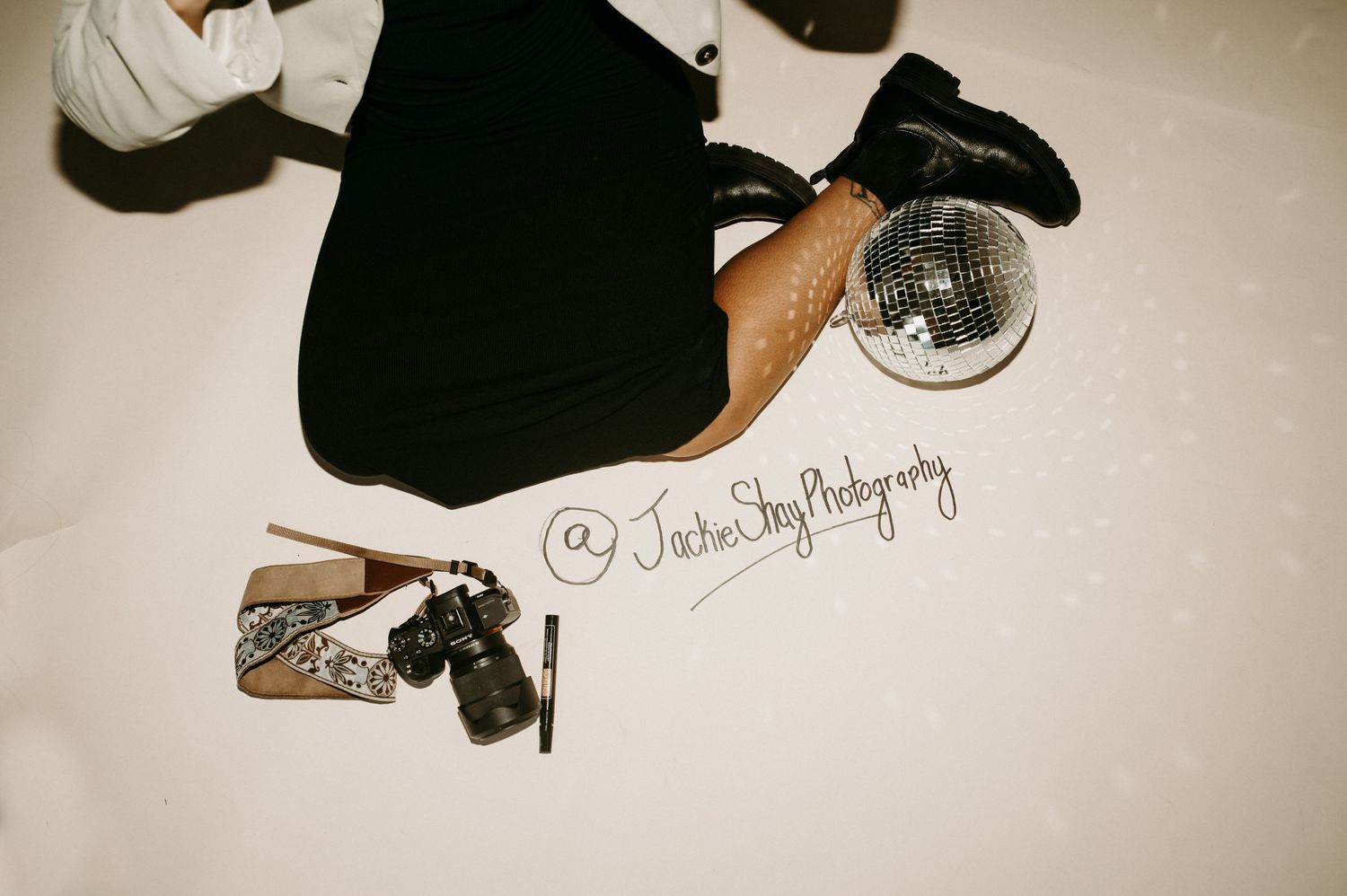 Overhead view of photographer with disco ball, camera and accessories on white floor.