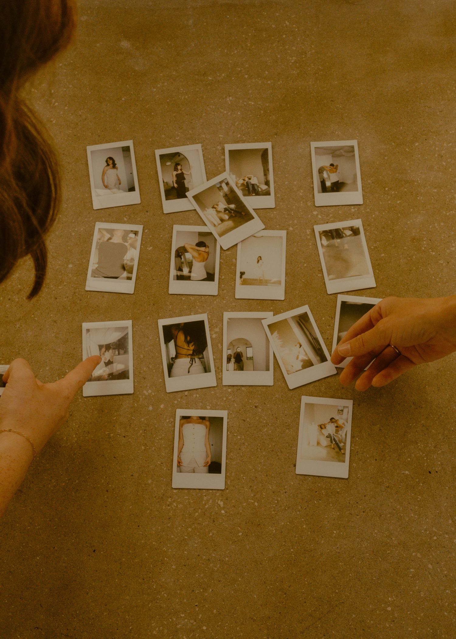 Two people arranging Polaroid instant photos on a textured surface, reviewing candid snapshots together.