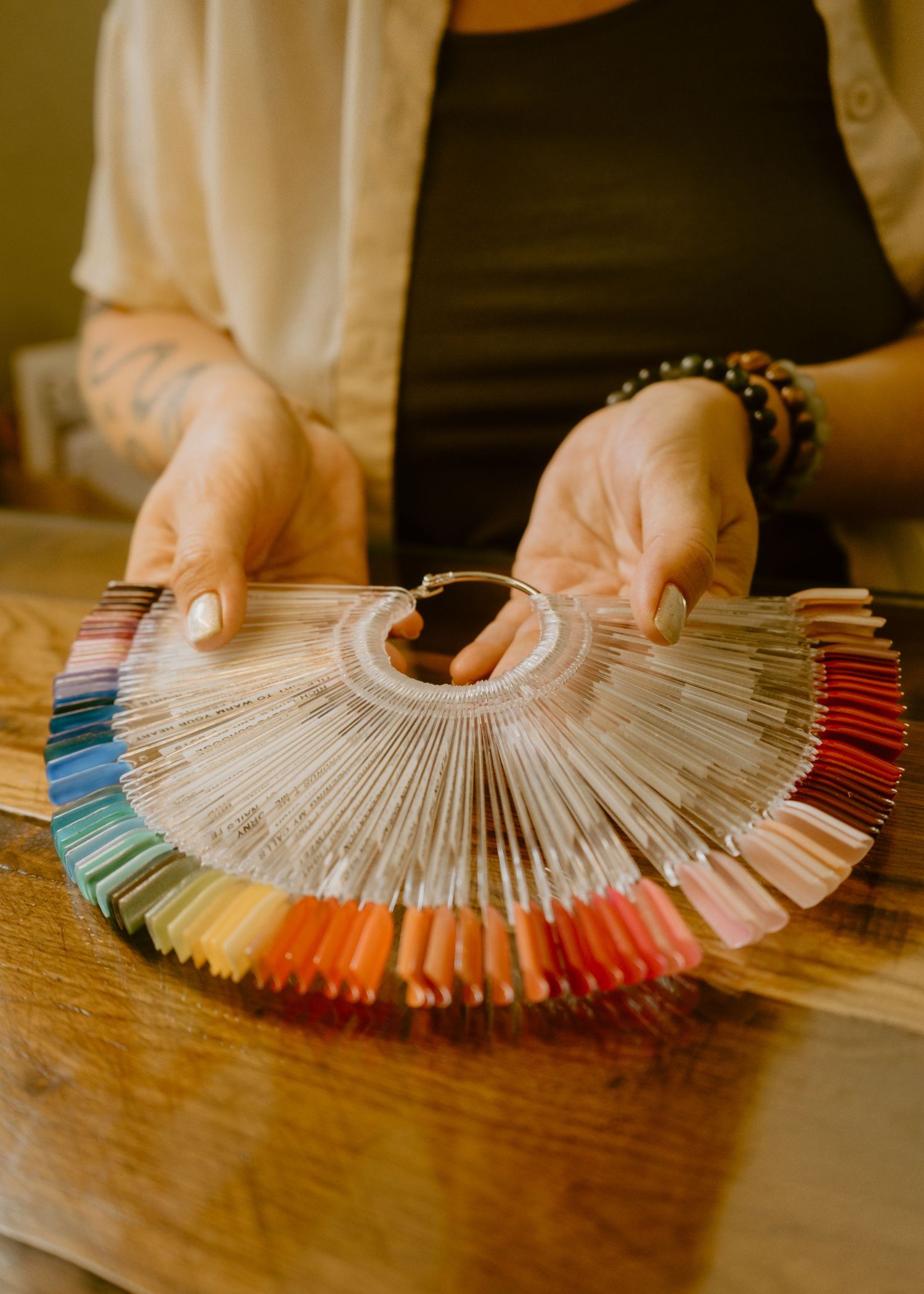 Person holding a fan-shaped nail polish color swatch display with rainbow gradient samples on a wooden table.