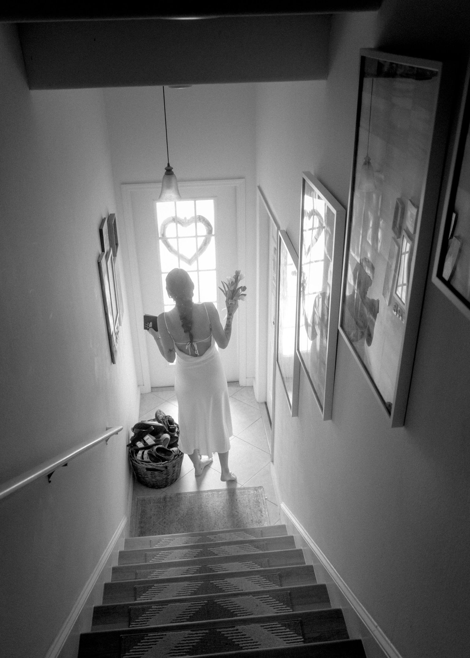 Black and white photo of a bride in white dress standing at bottom of stairs near heart-decorated door.