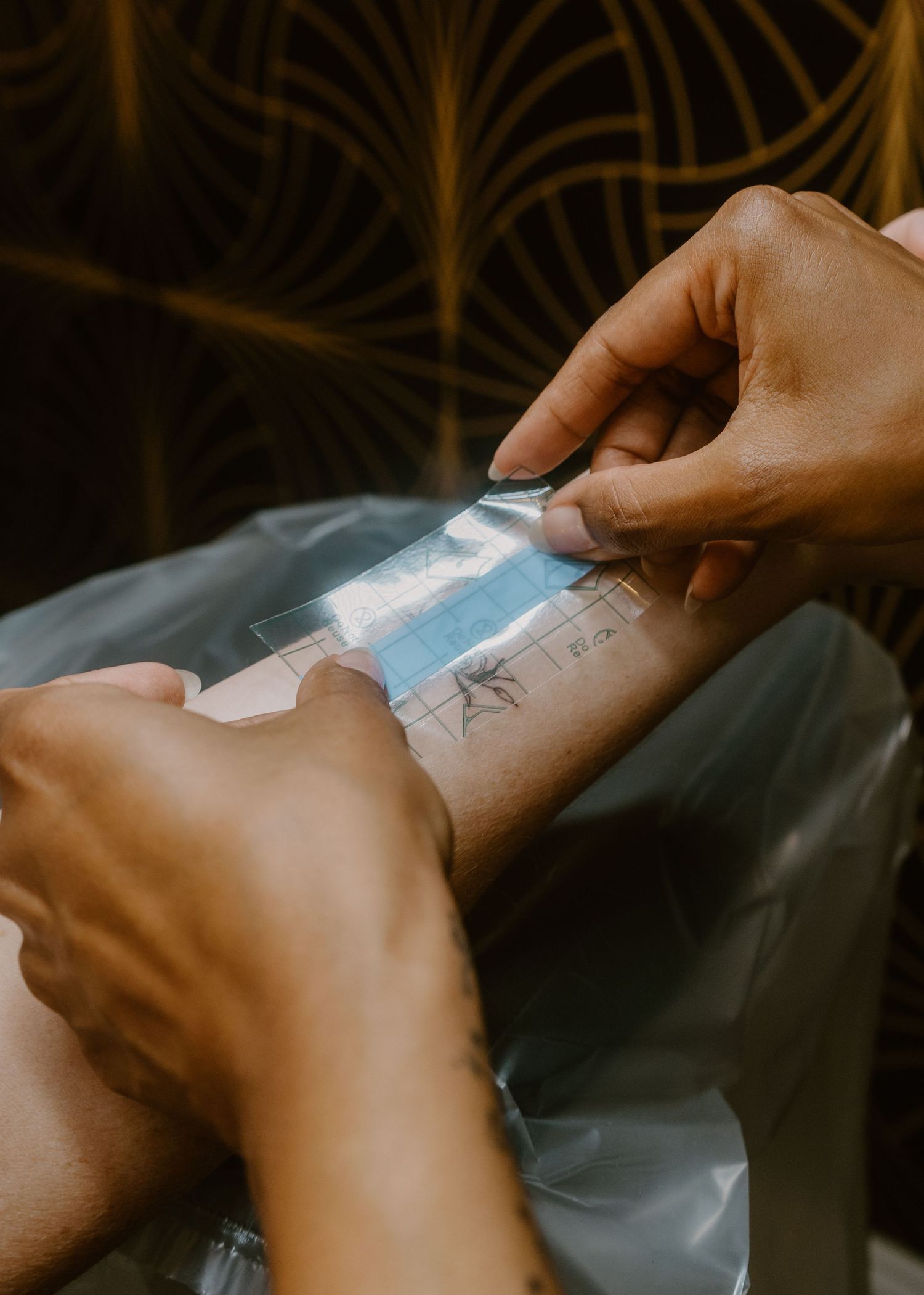 Tattoo artist applying a stencil transfer to a client's forearm before tattooing.