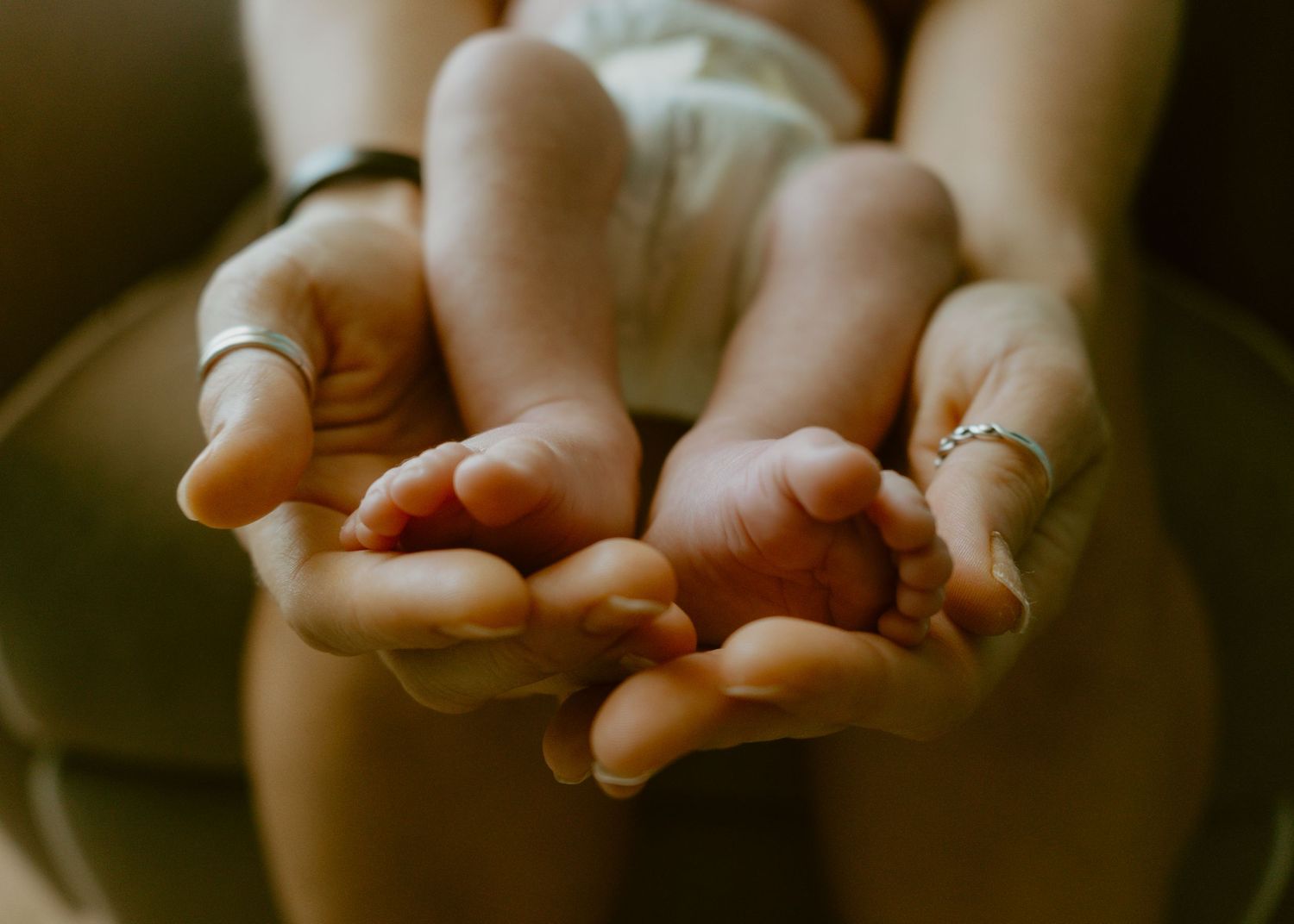 Close-up of a mother's hands cradling tiny newborn baby feet, wearing a silver ring.