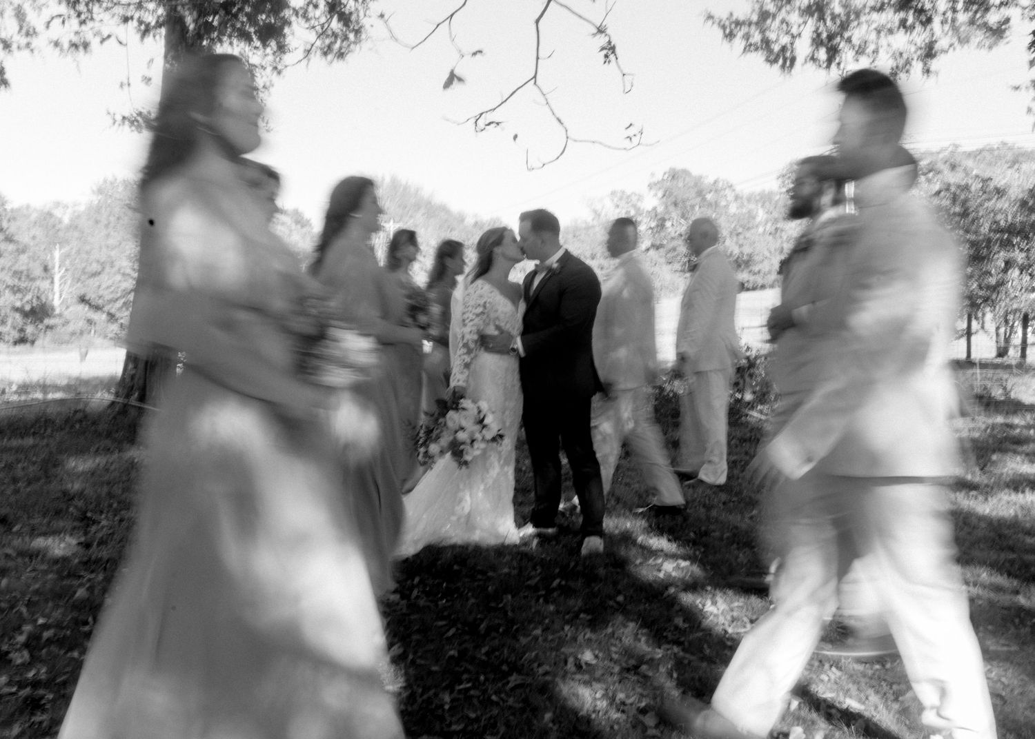 Artistic blurred black and white photo of wedding party gathered under trees.