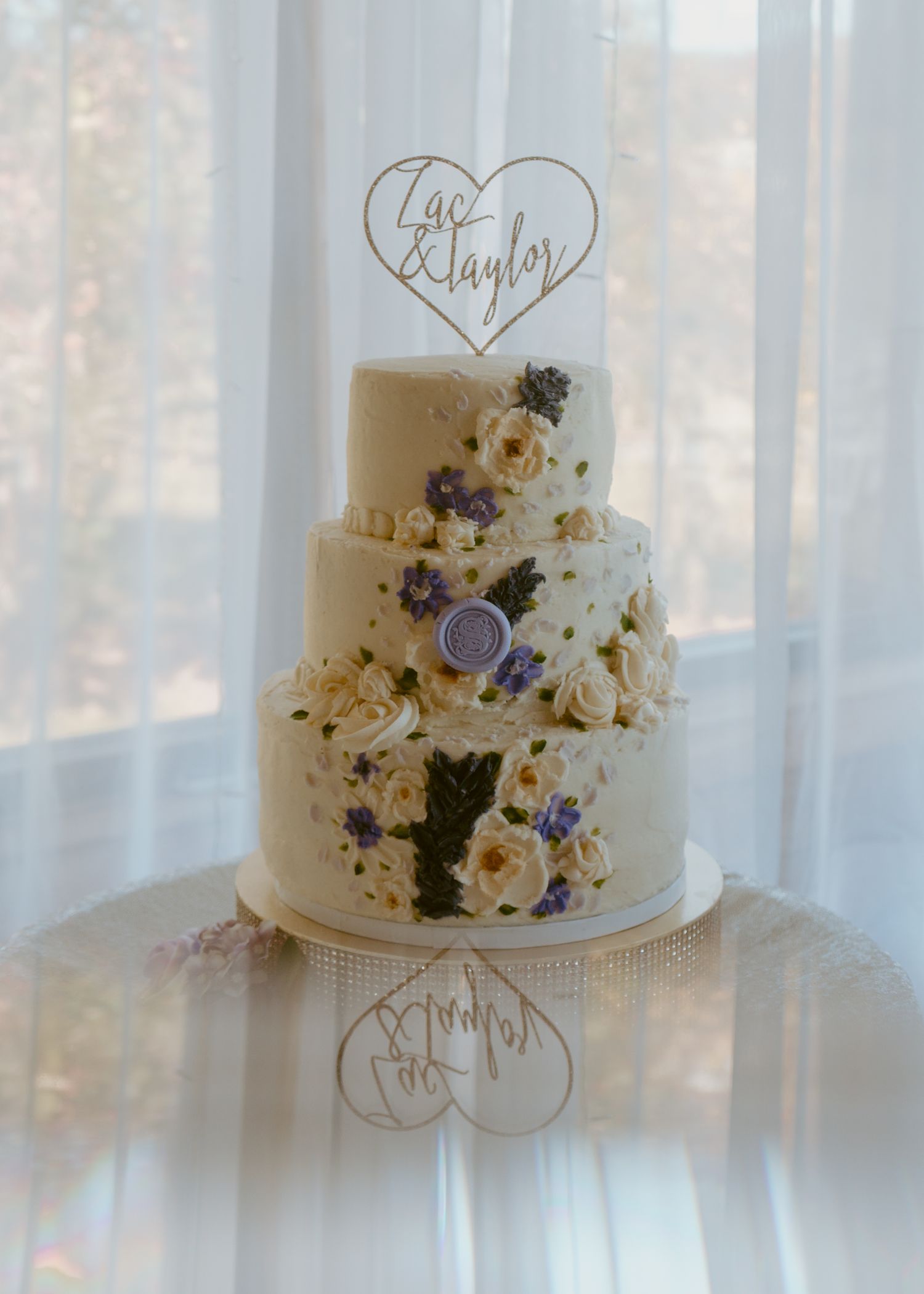Three-tier white wedding cake with purple and cream floral decorations and a heart-shaped 