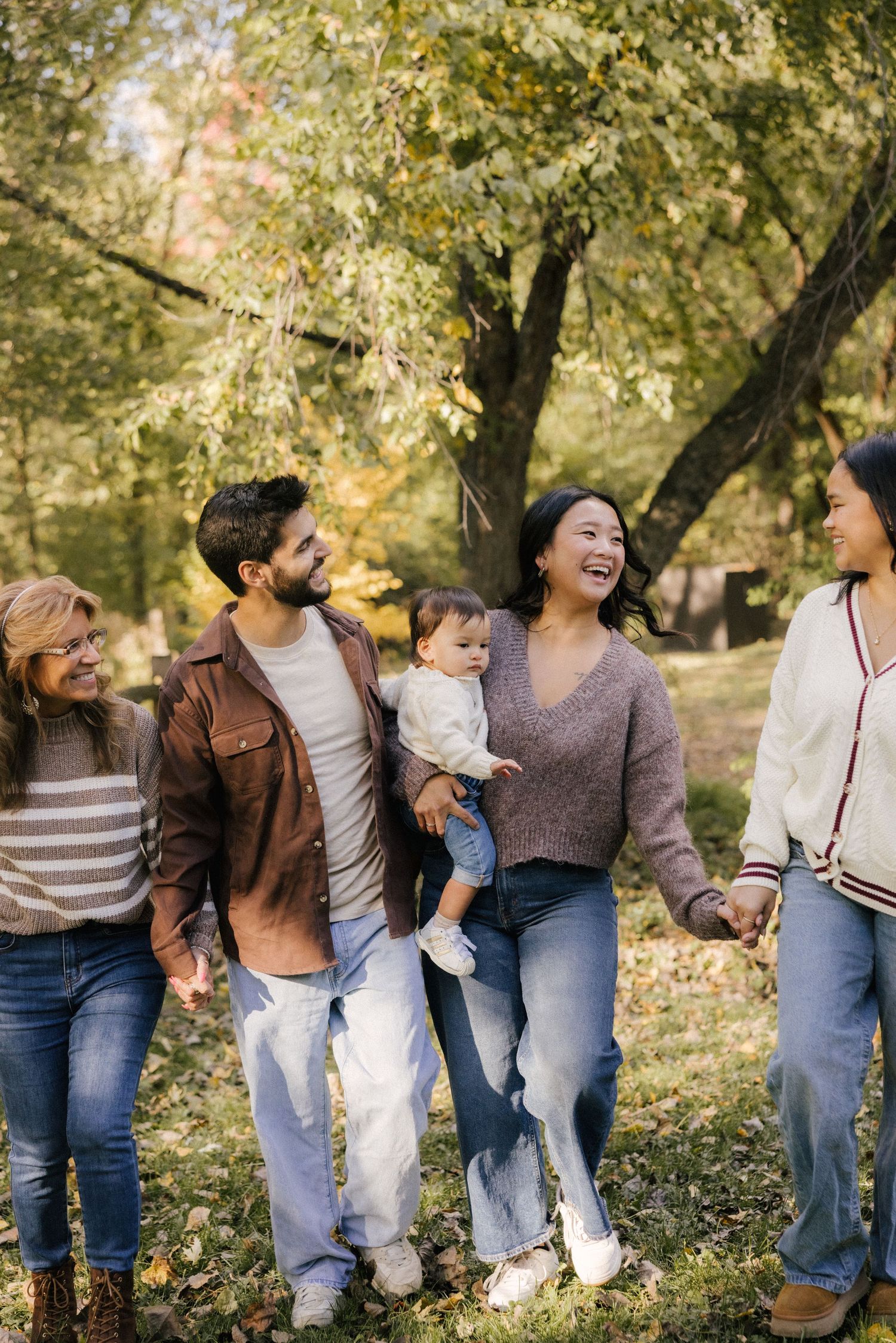 Group of friends walking together and laughing in a park during autumn with golden leaves on trees.
