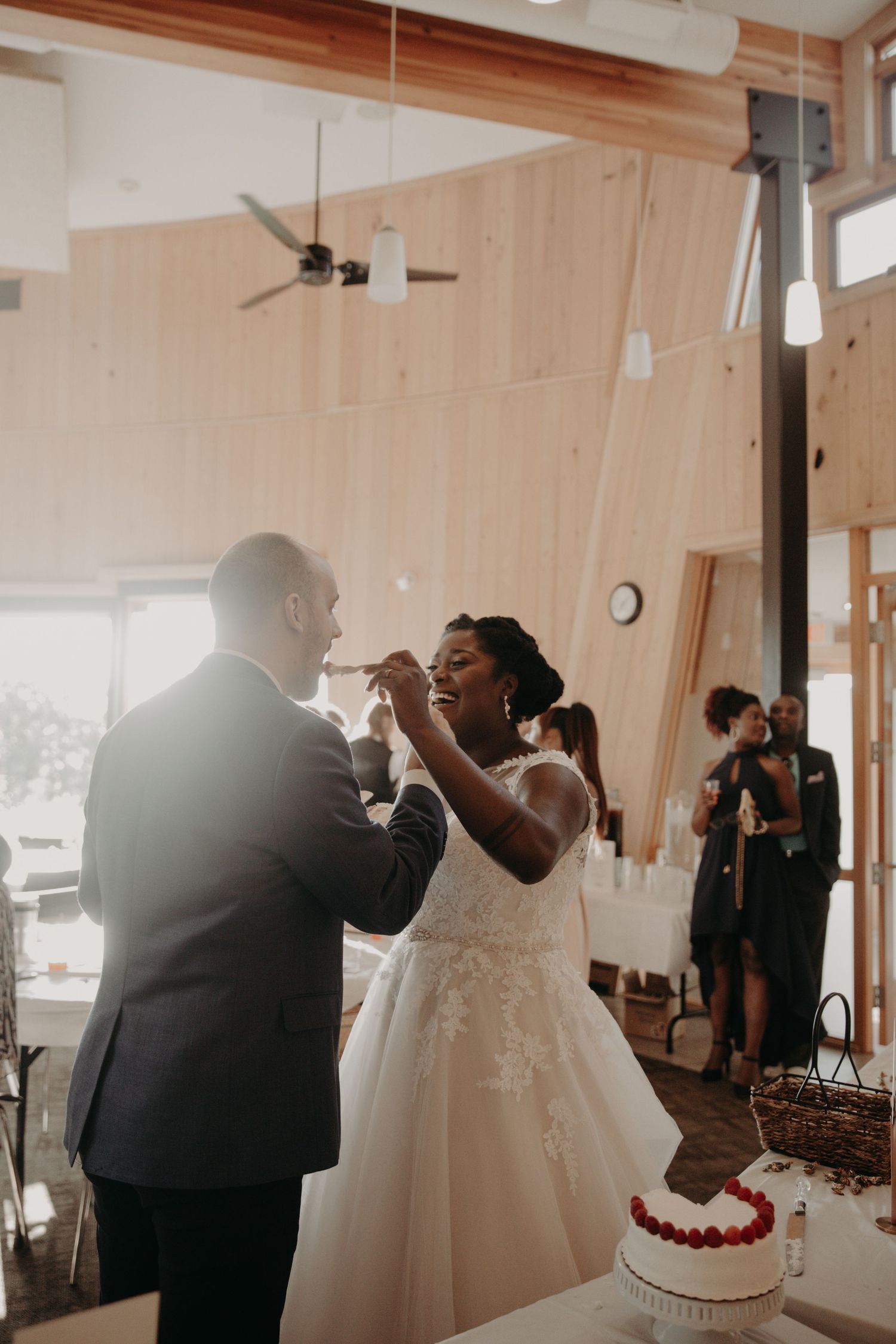 Newlyweds sharing first bite of wedding cake during reception celebration.