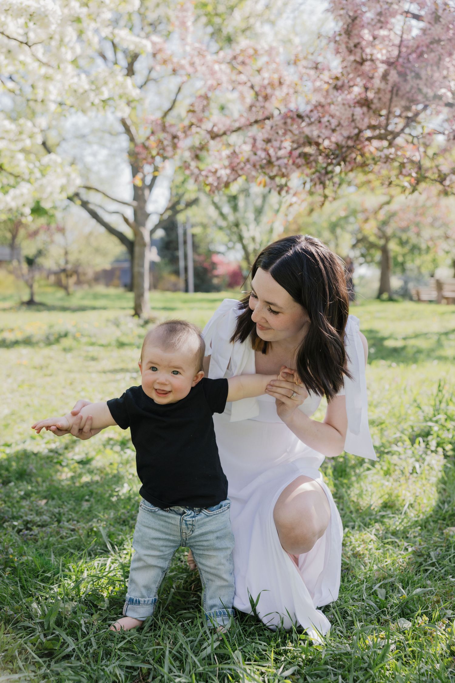 Mother and toddler share joyful moment under blooming cherry blossom trees in spring garden.