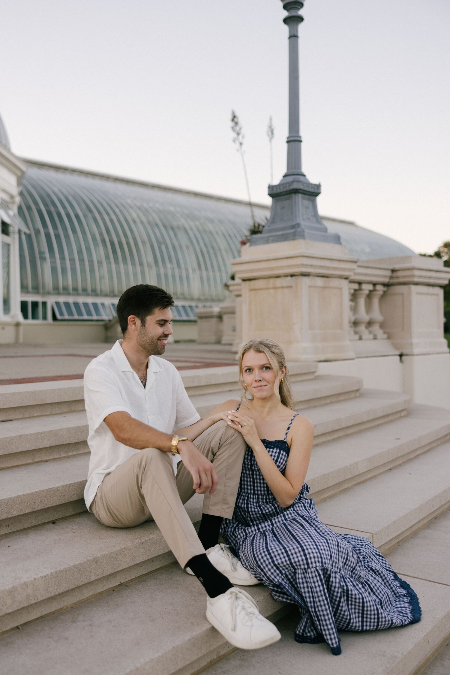 A couple sits and chats on outdoor marble steps with an ornate architectural backdrop.
