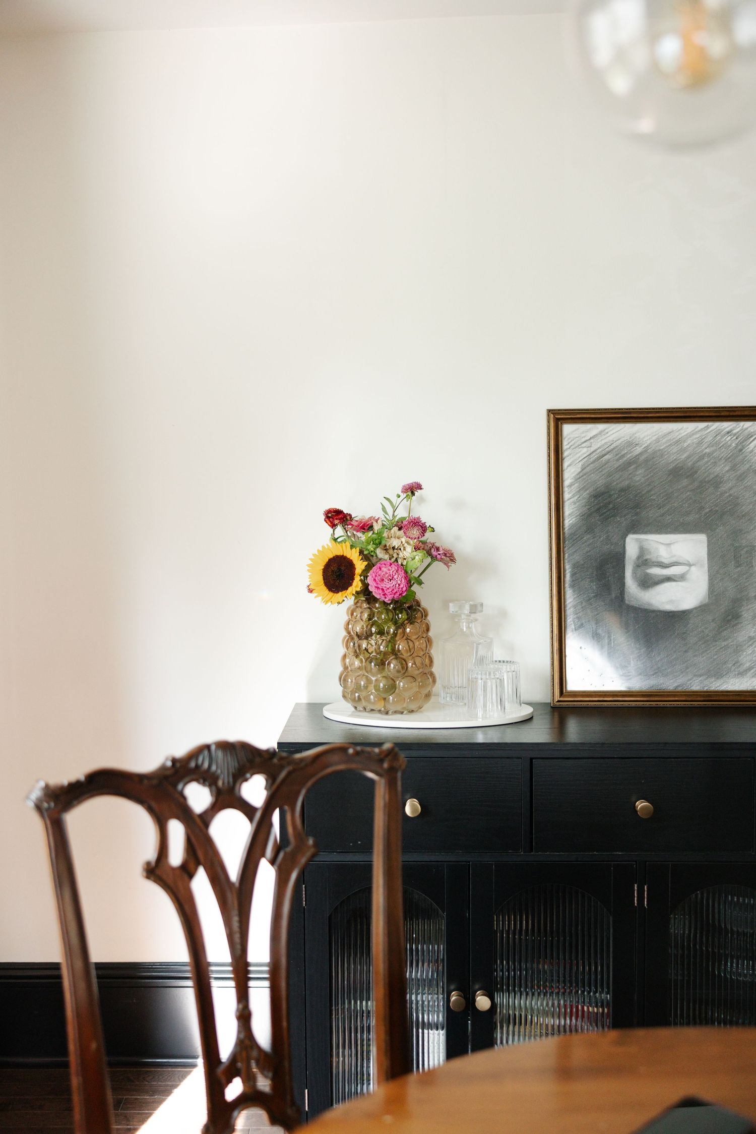 A rustic dining room setup with dark wooden chairs and a white floral cake displayed on a decorative cabinet.