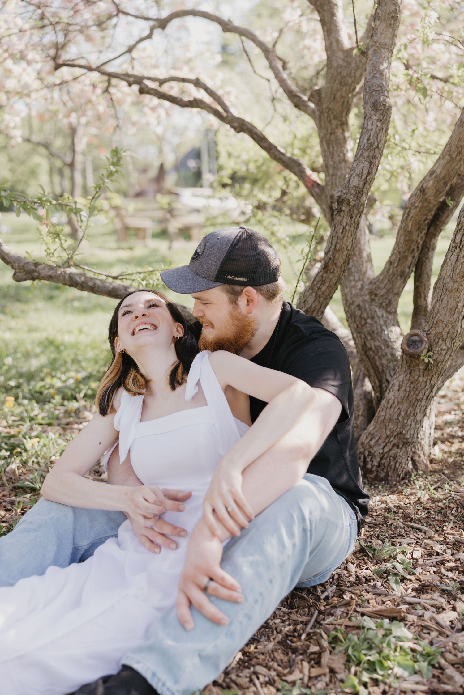 Couple sharing a tender romantic moment while sitting beneath blooming spring trees in a garden setting.