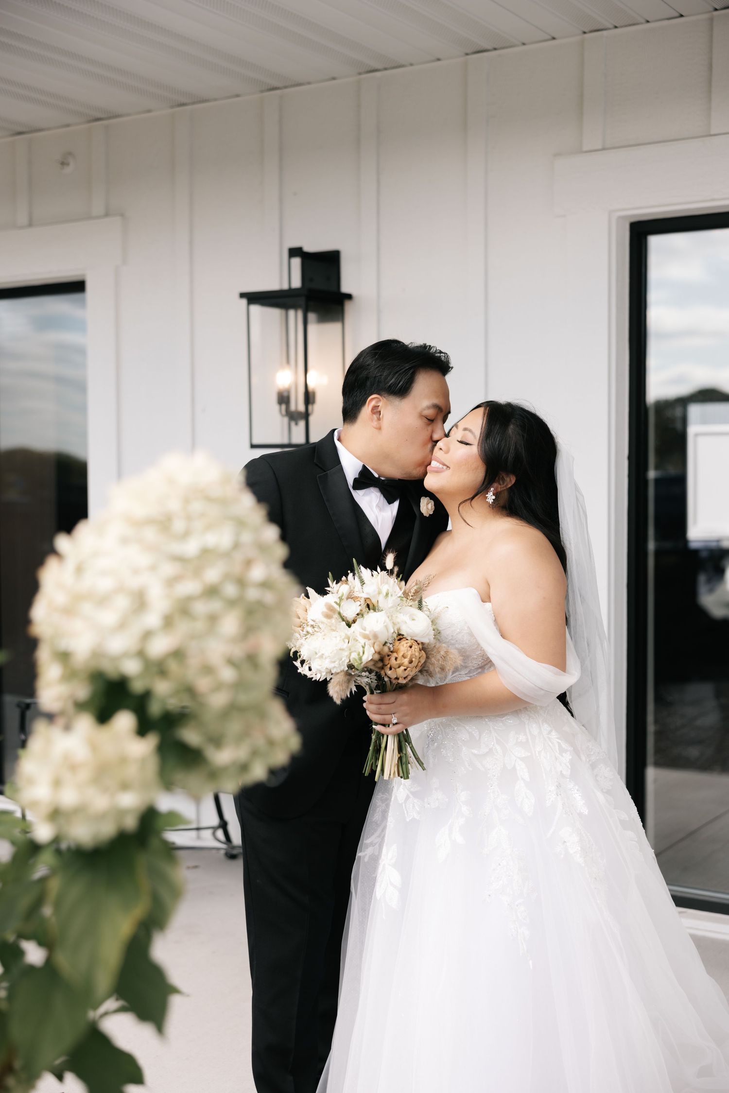 A romantic wedding moment captured in a white room with elegant white floral bouquets and decor.