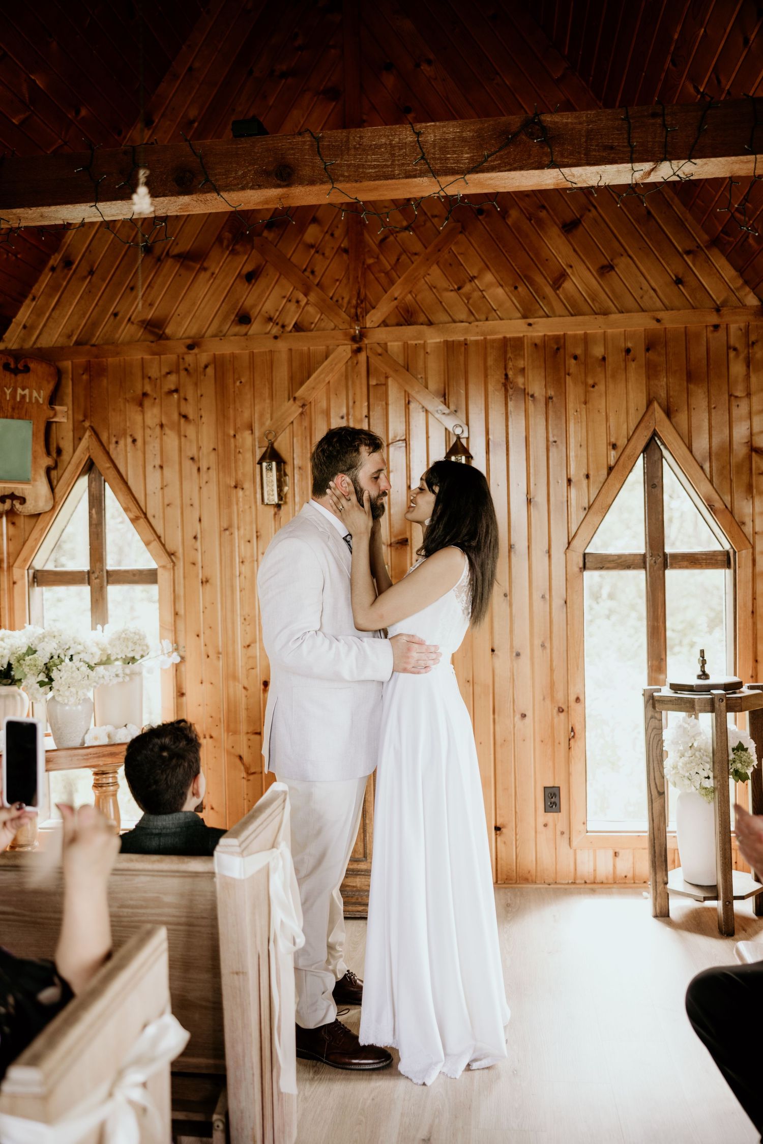 Romantic wedding ceremony takes place in a rustic wooden chapel with triangular windows and warm lighting.
