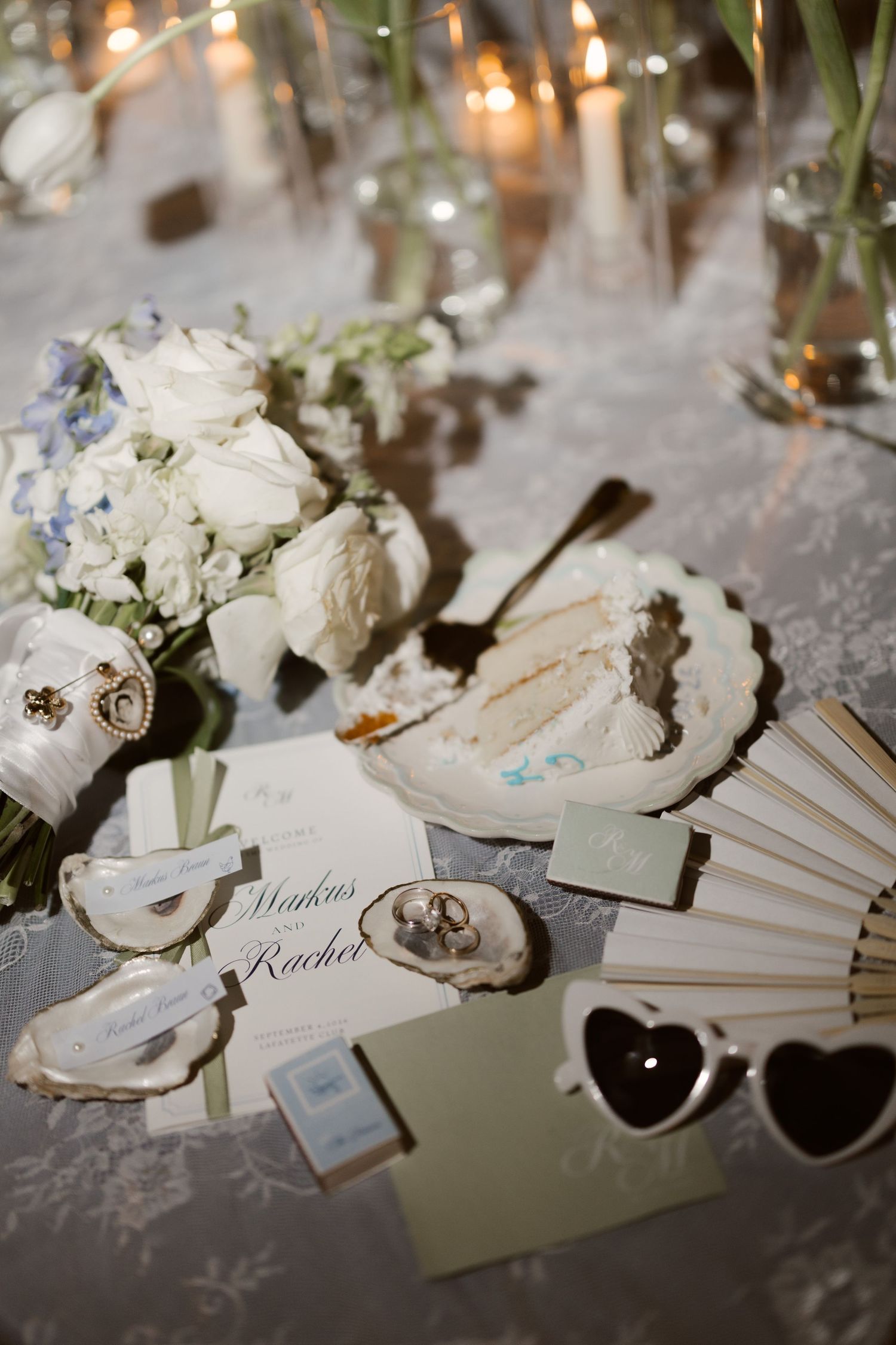 Elegant wedding table with white roses, oyster shells, heart sunglasses, a hand fan, and candlelight decor.