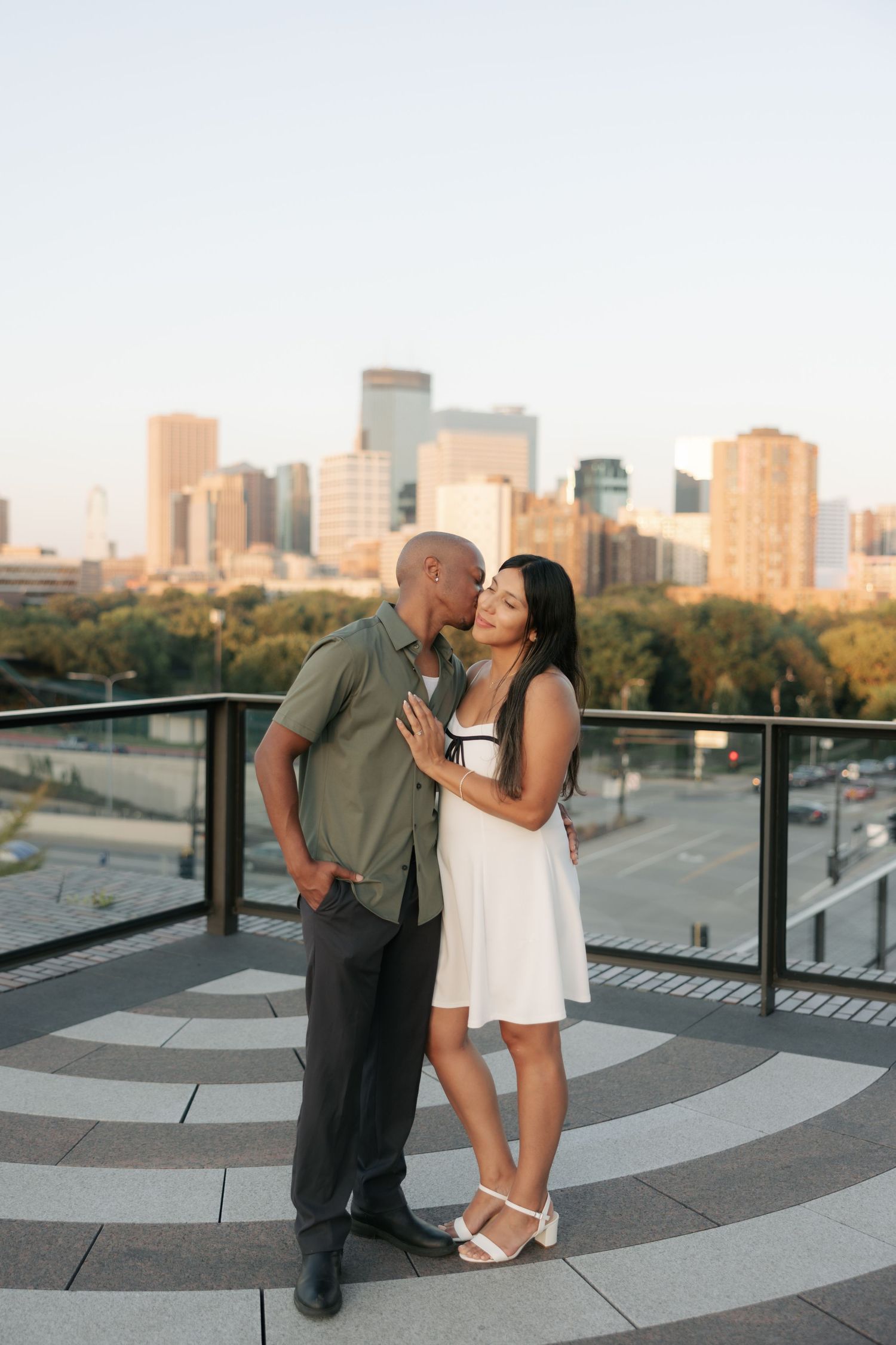 A couple shares a romantic moment on a rooftop terrace overlooking the Minneapolis skyline at sunset.