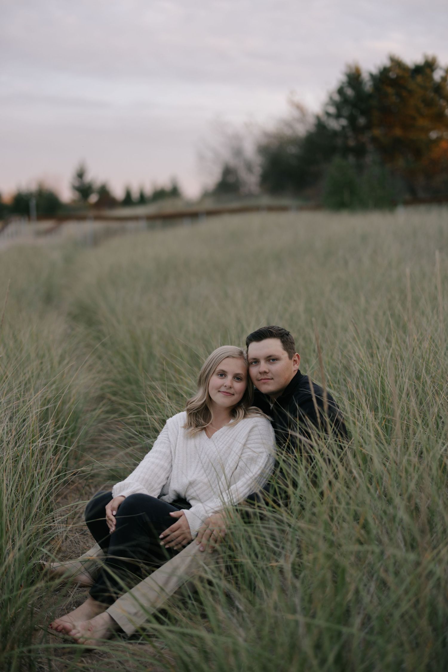 A couple relaxes together in tall grass during a romantic outdoor photo session at sunset.