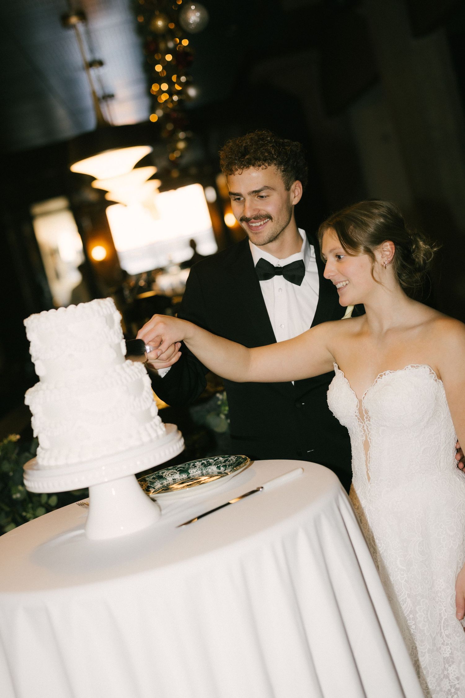Newlywed couple cutting their elegant white tiered wedding cake together at their reception celebration.
