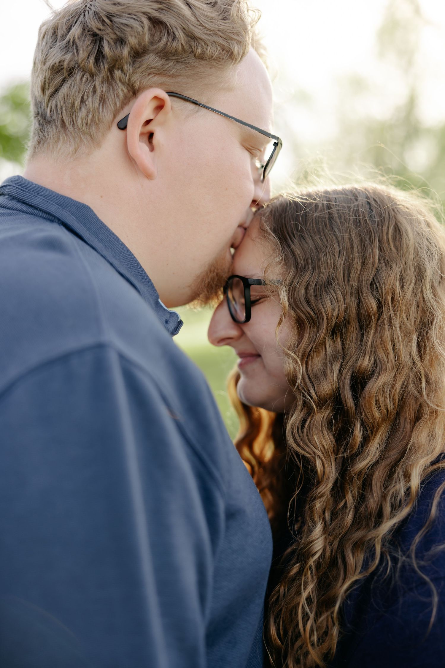 A tender romantic moment between a couple wearing glasses and dark shirts as they share an intimate gesture.