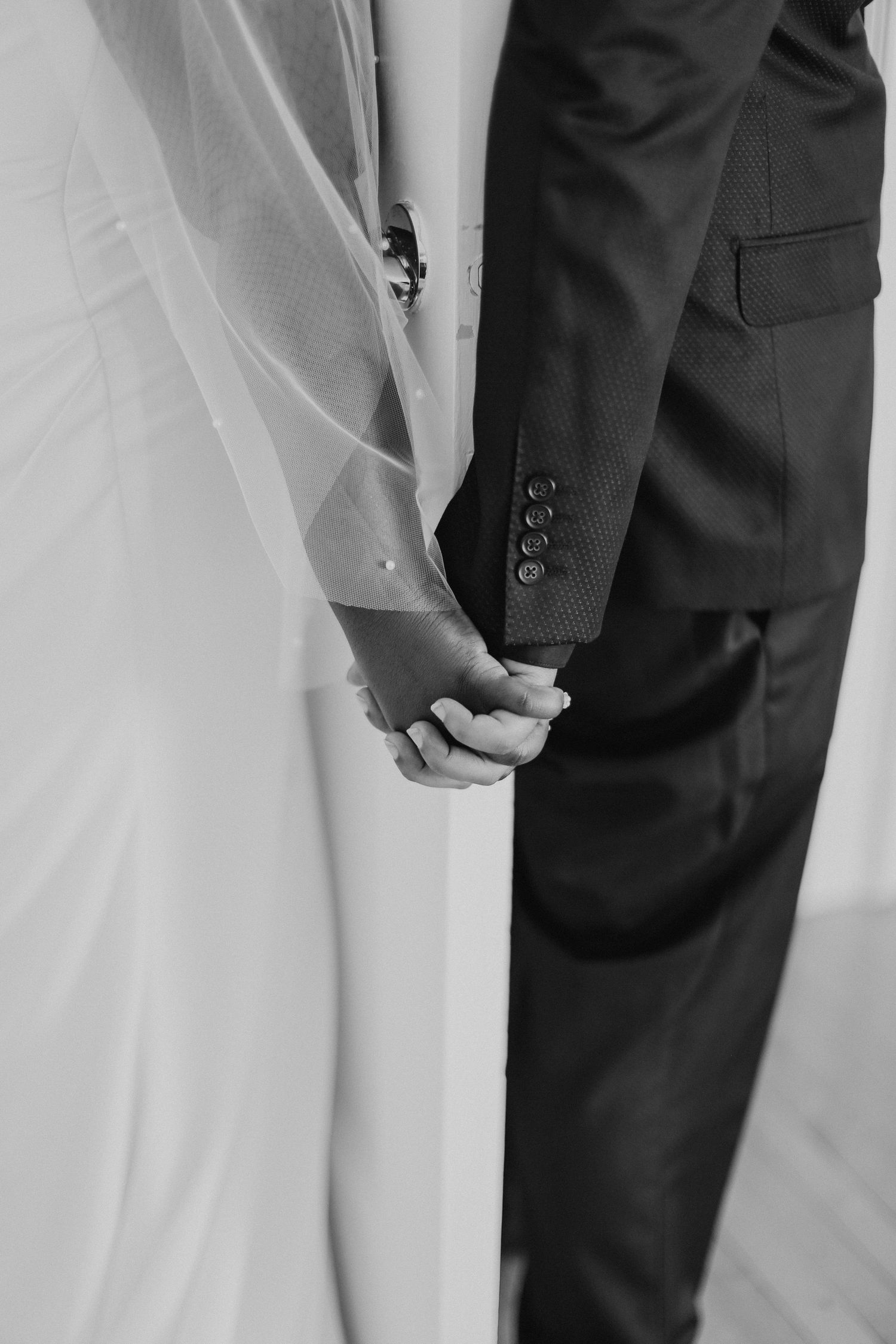 A black and white close-up of a bride and groom holding hands during their wedding ceremony.