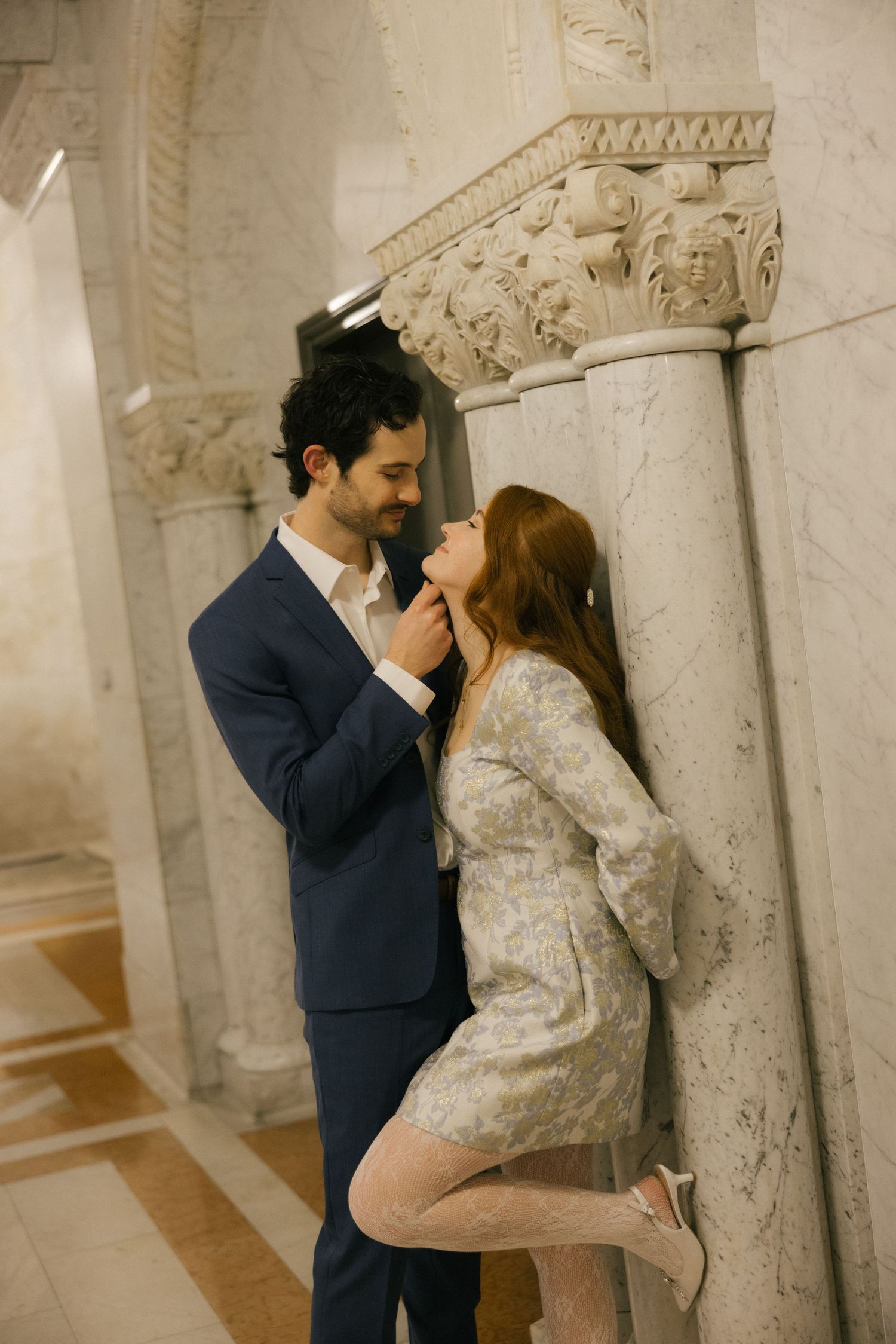 Romantic wedding couple embraces in an elegant stone corridor with ornate architectural details and soft lighting.