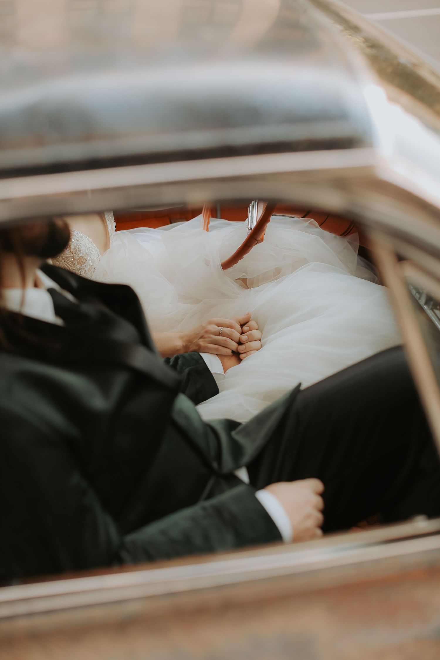 Intimate view of a couple's clasped hands inside a car on their wedding day.