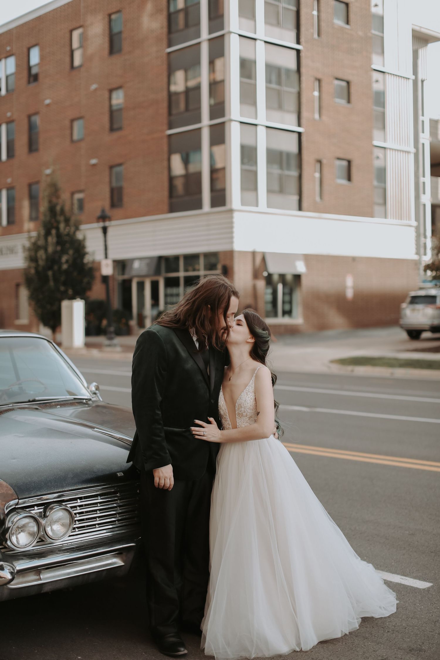 Romantic wedding couple sharing a moment next to a vintage car on a city street.