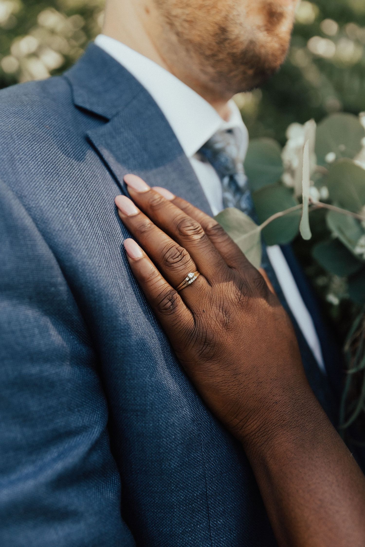 Close-up of a dark-skinned hand with wedding ring resting on a navy blue suit jacket.