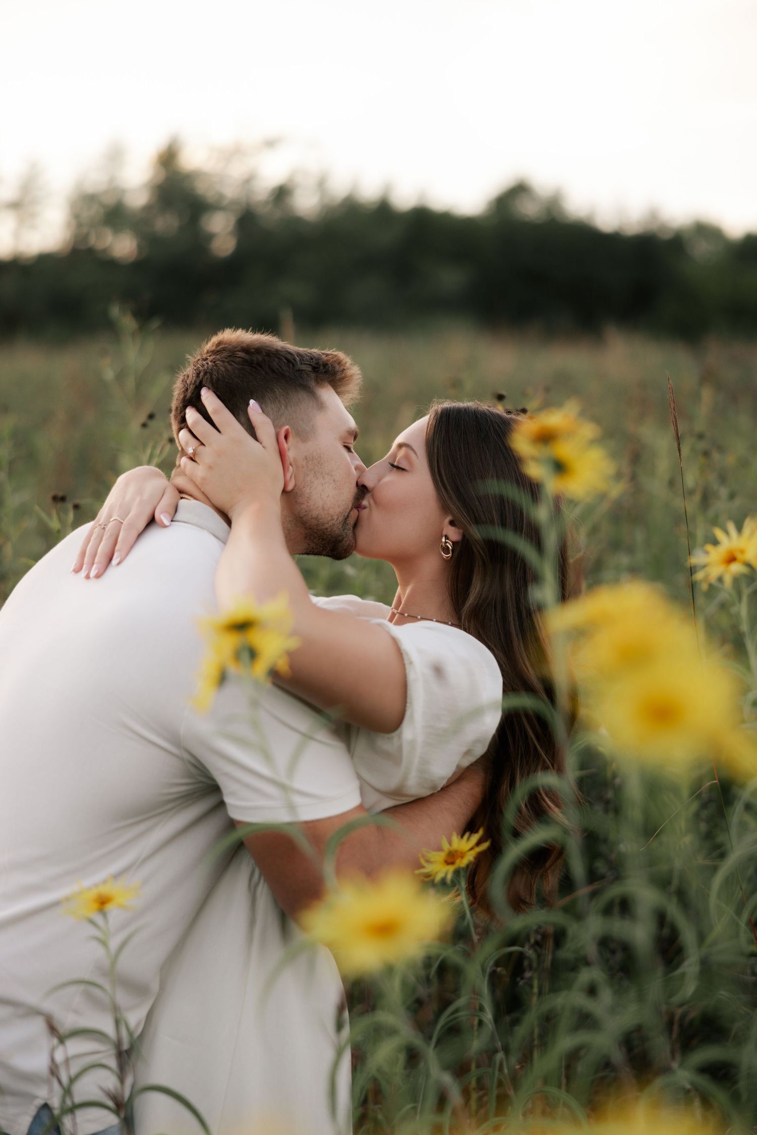 A romantic kiss shared between a couple in a field of blooming yellow sunflowers at sunset.