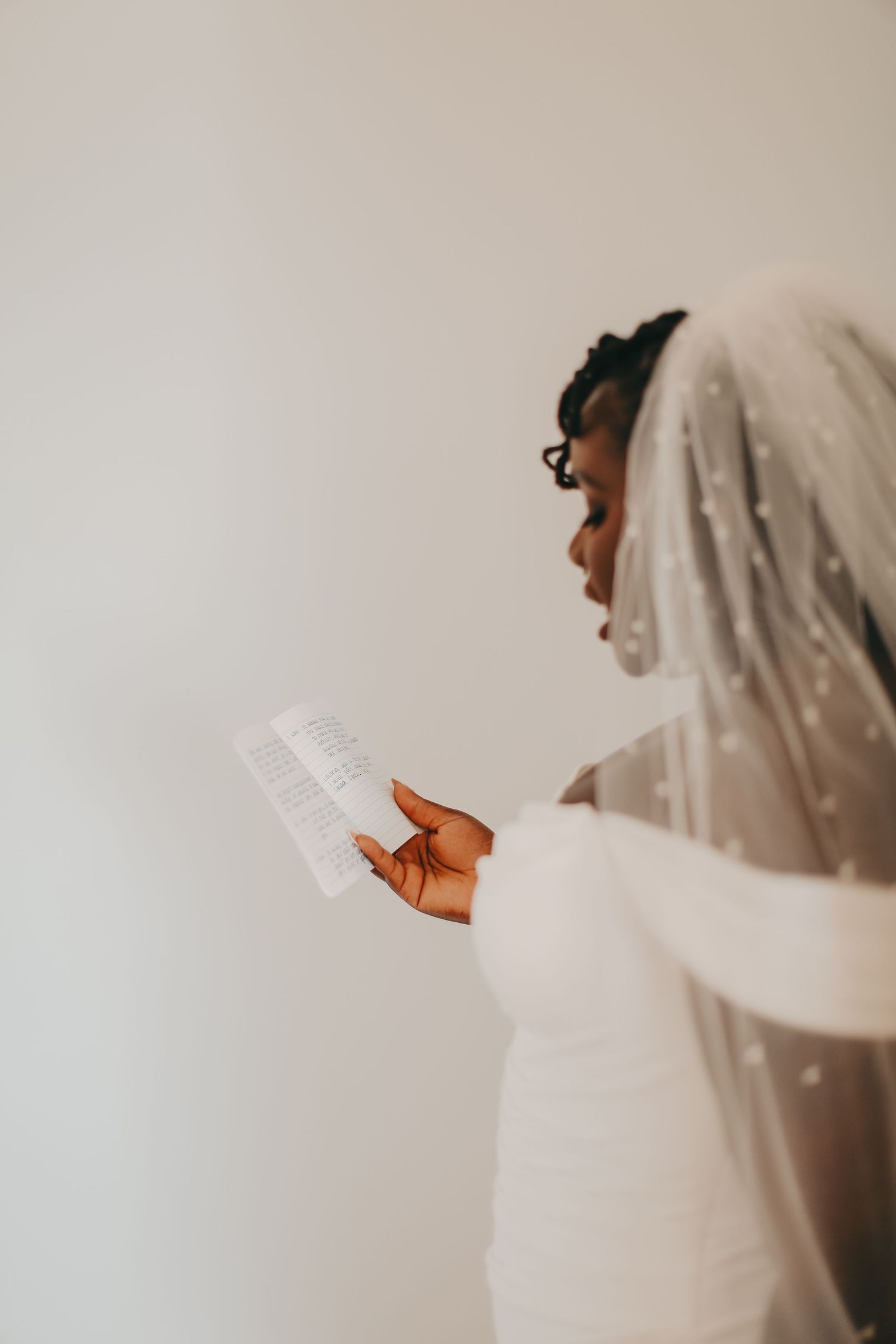 Bride in white dress reads a note while her veil flows in the natural light.
