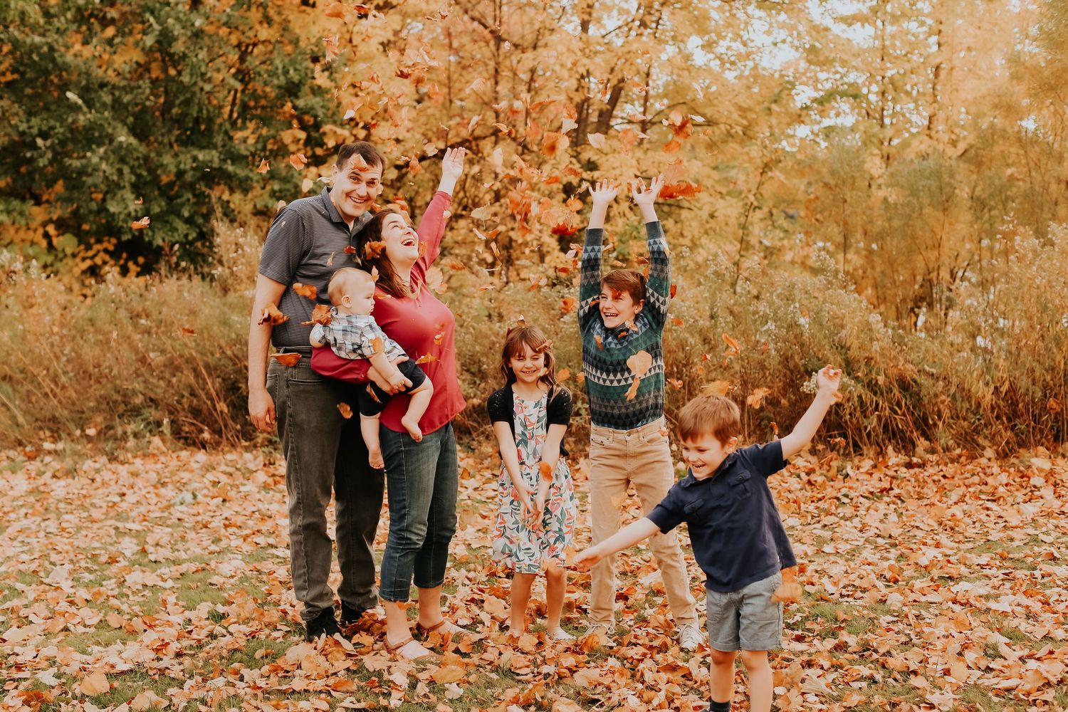 A family plays together in a pile of fallen autumn leaves on a crisp fall day.