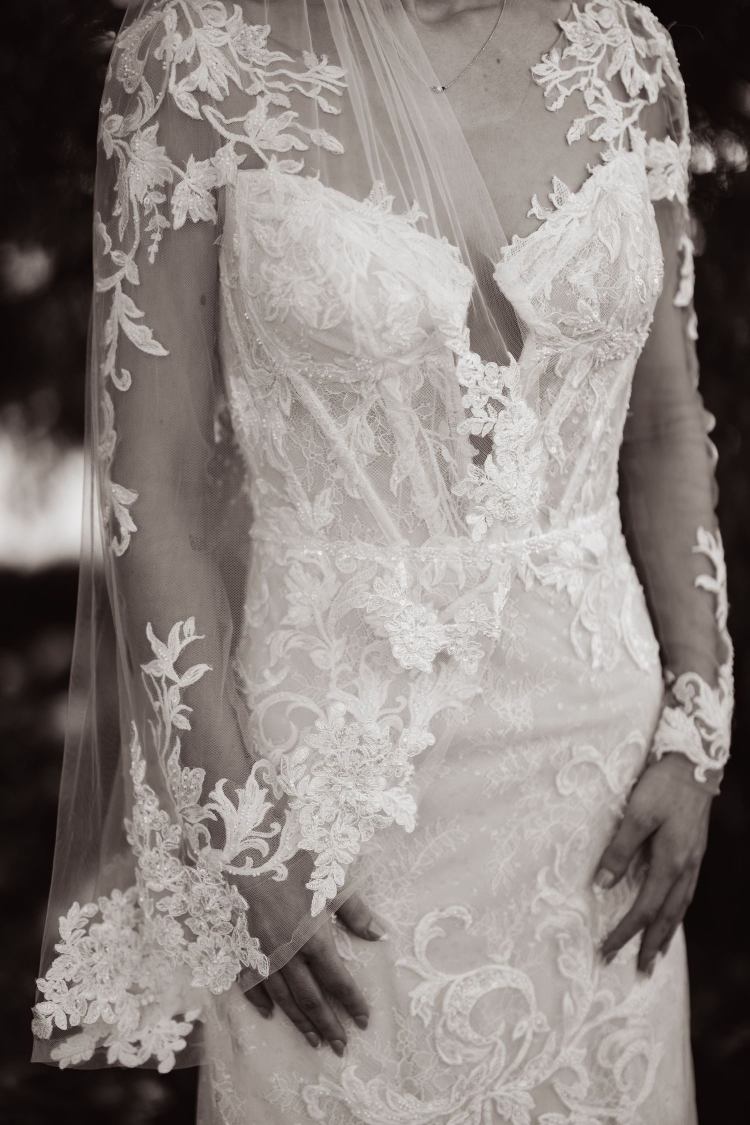 Close-up details of delicate white lace appliques and embroidery on a wedding dress bodice in black and white.