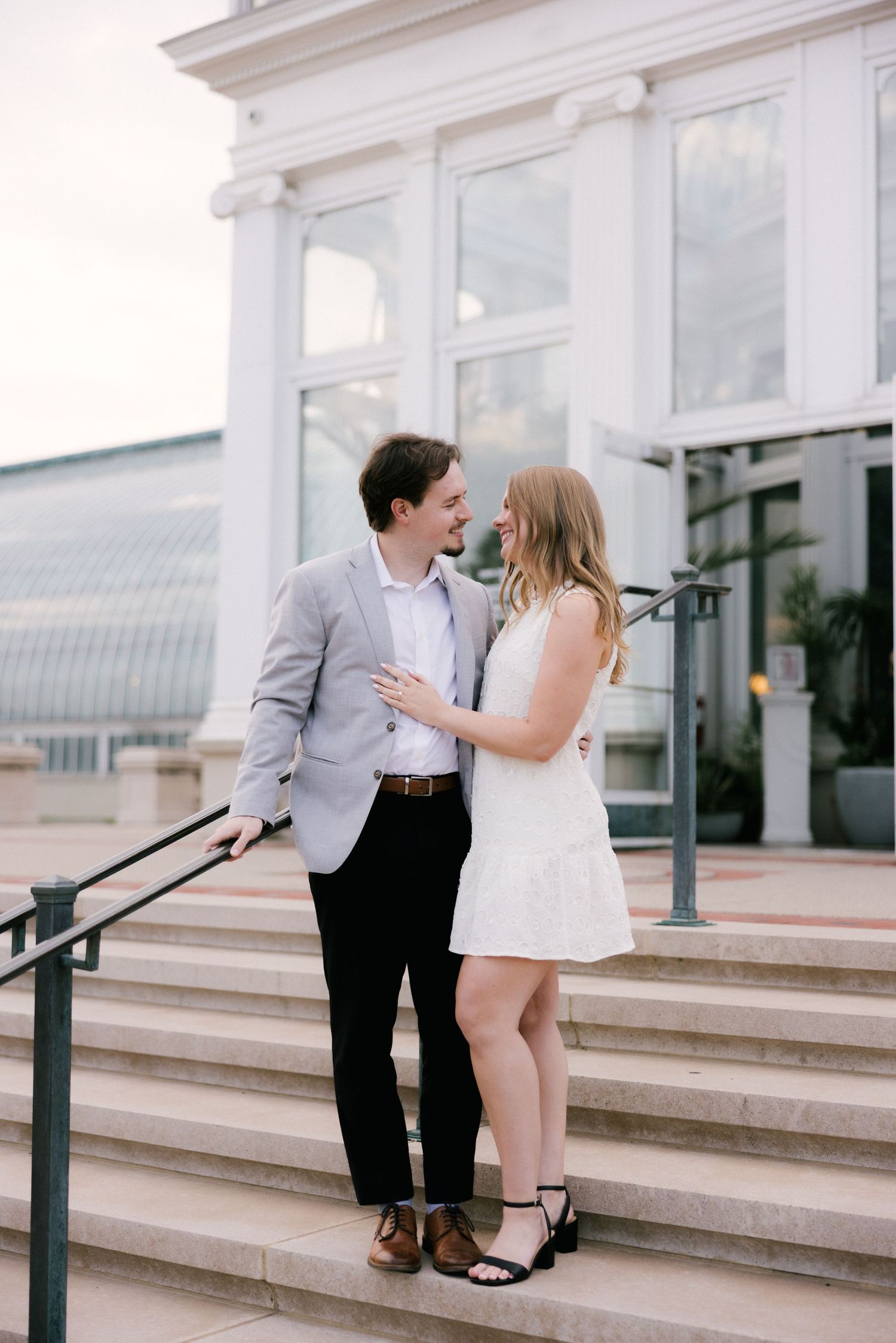 A couple shares a romantic moment on white marble steps outside an elegant building.