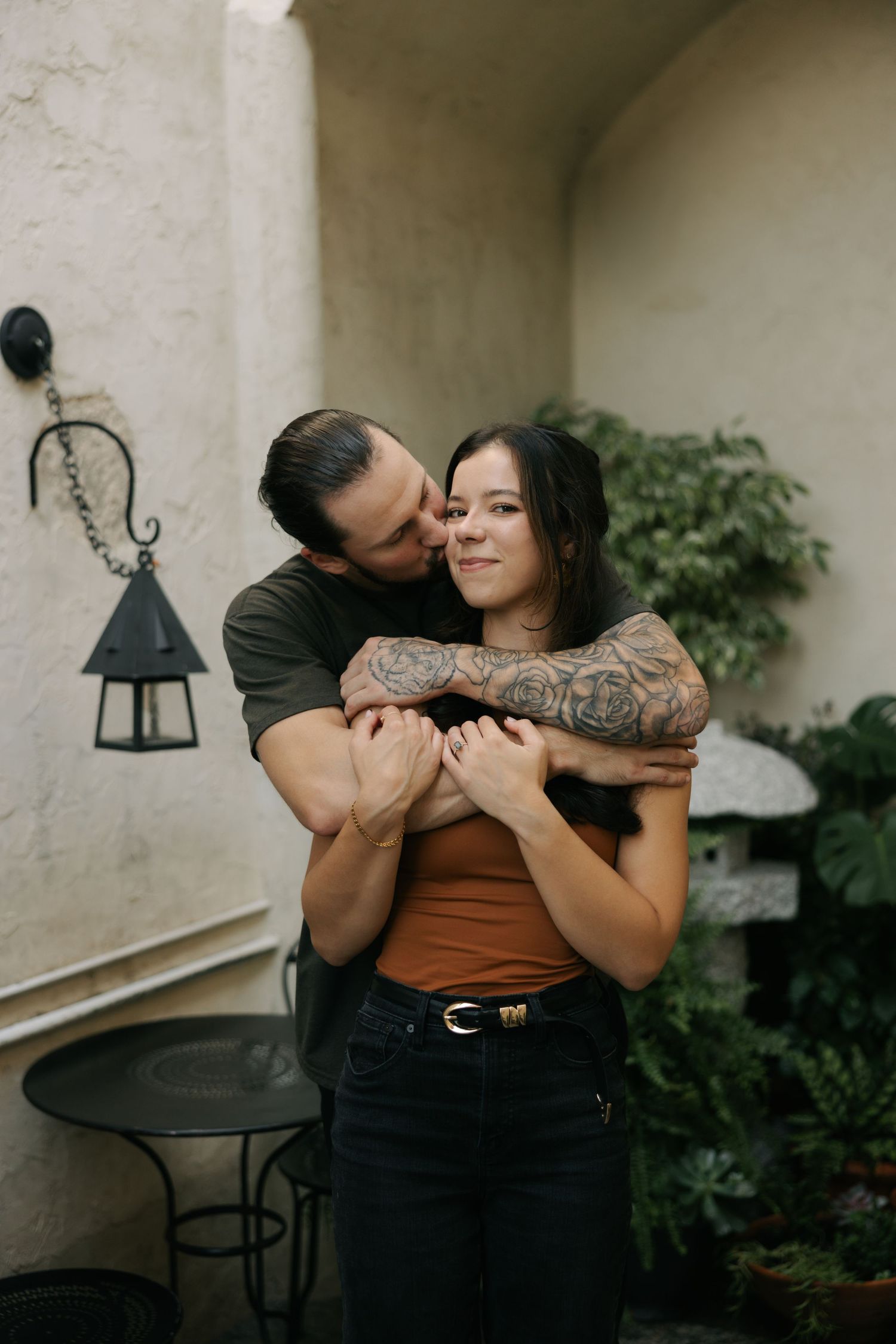 A romantic couple shares intimate moments in a series of four candid photos against a white wall and patio setting.