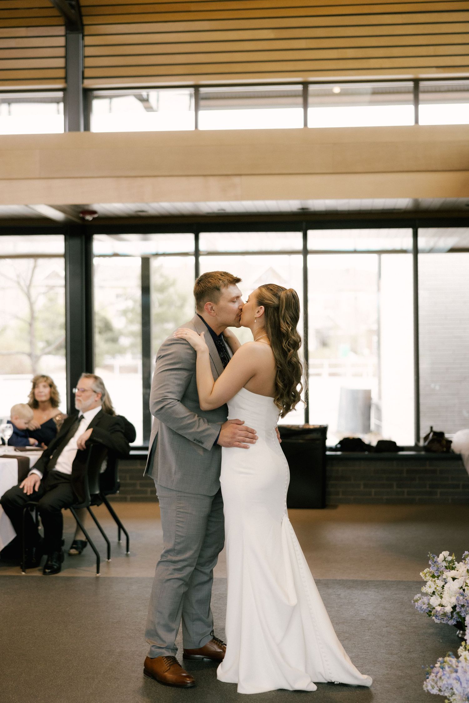 Bride and groom share their first kiss as a married couple during their wedding reception in a modern venue.