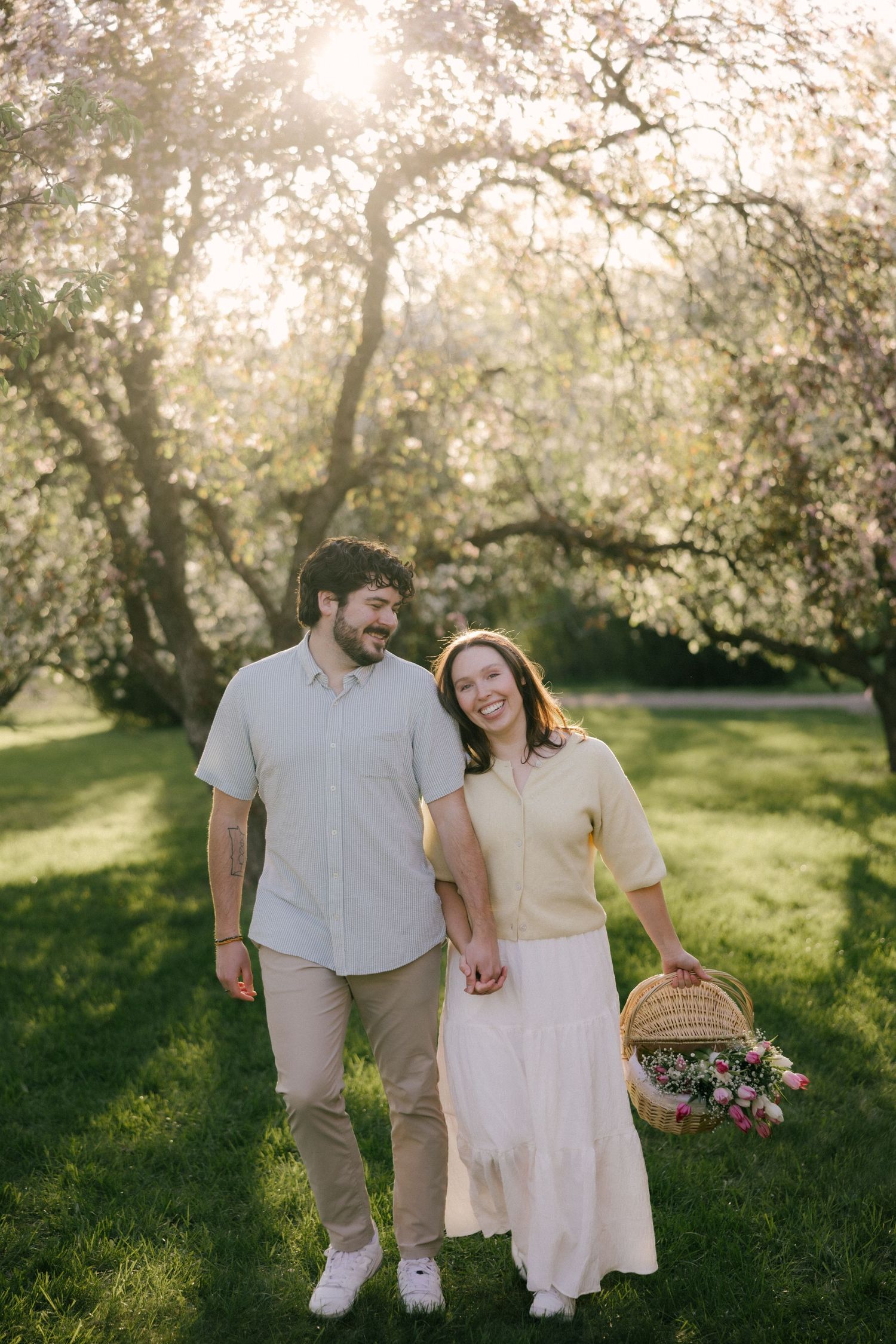 Happy couple walking hand in hand through a sunny blossoming park, woman carrying a flower basket.