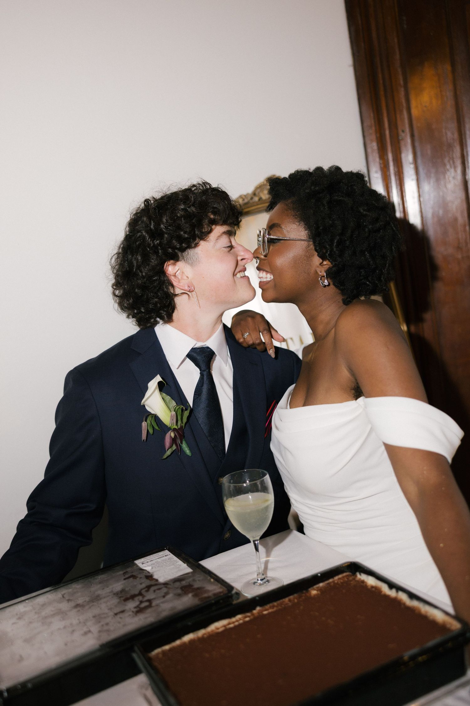 Interracial couple sharing a romantic moment at their wedding reception, bride in white dress, groom in navy suit.