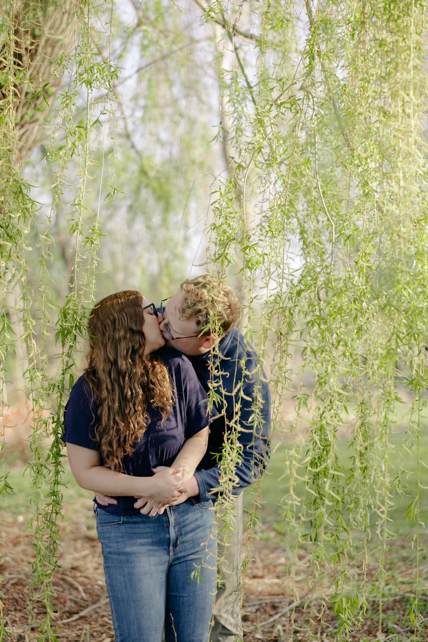 A romantic moment captured under cascading willow branches in soft springtime light.