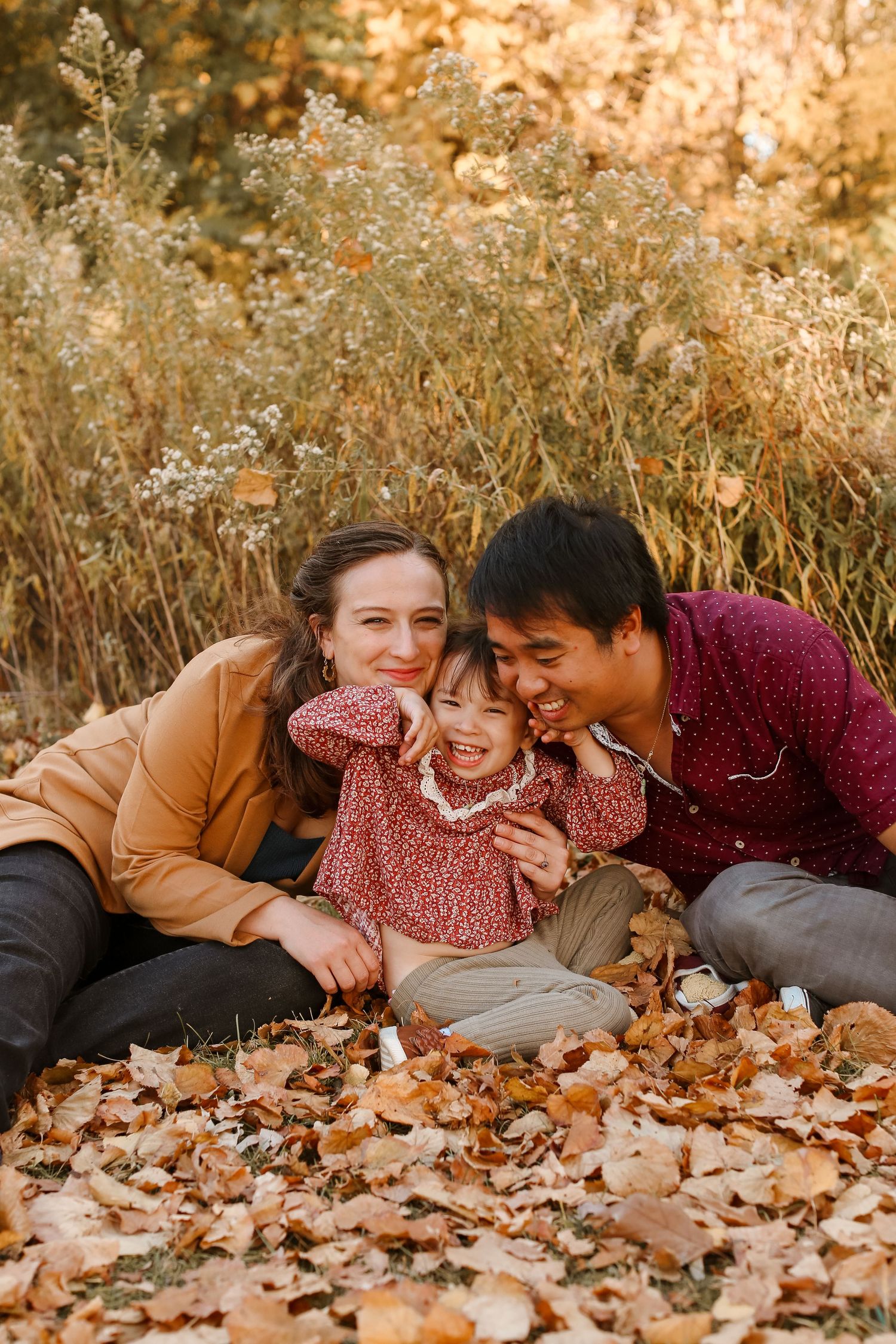 Family lying together on autumn leaves during golden hour photo session.