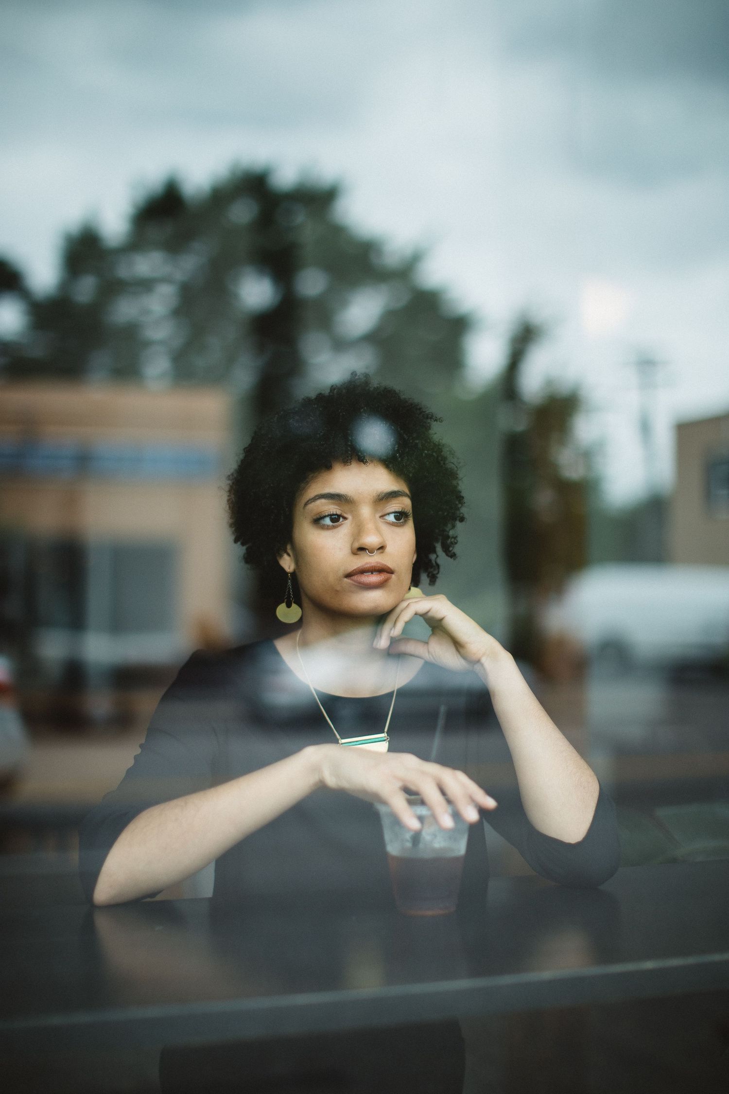 A stylish person with natural hair gazes contemplatively through a window in an artistic portrait.
