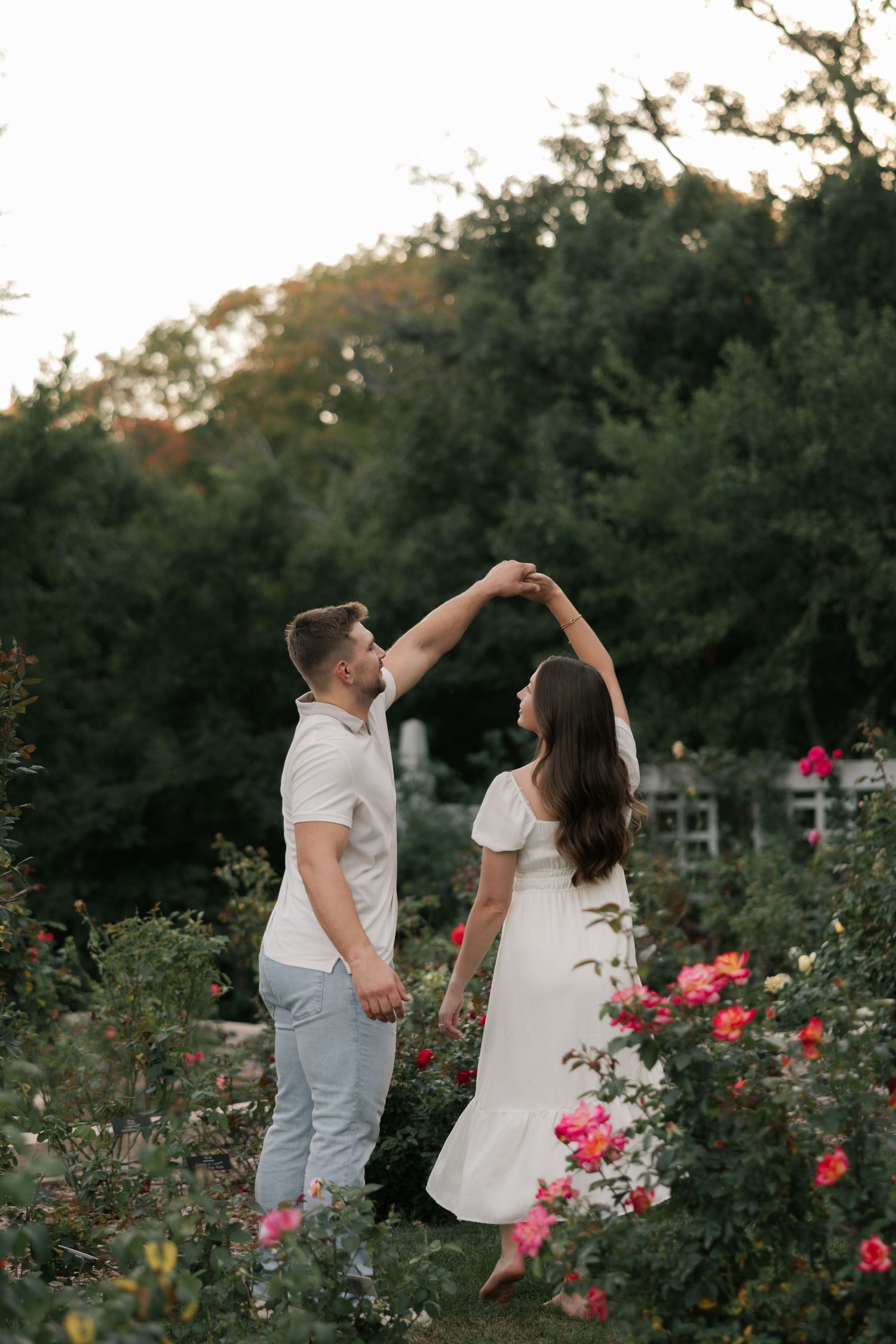 A couple dances together in a romantic garden setting surrounded by blooming pink roses at dusk.