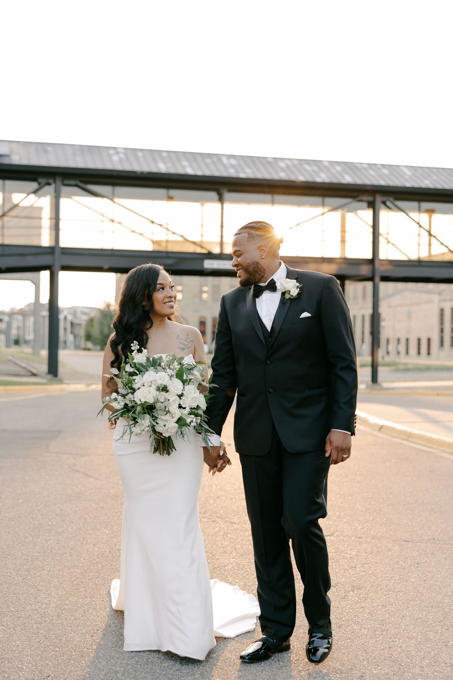 A modern wedding couple poses for stylish portraits during a sunset shoot at an industrial train station location.