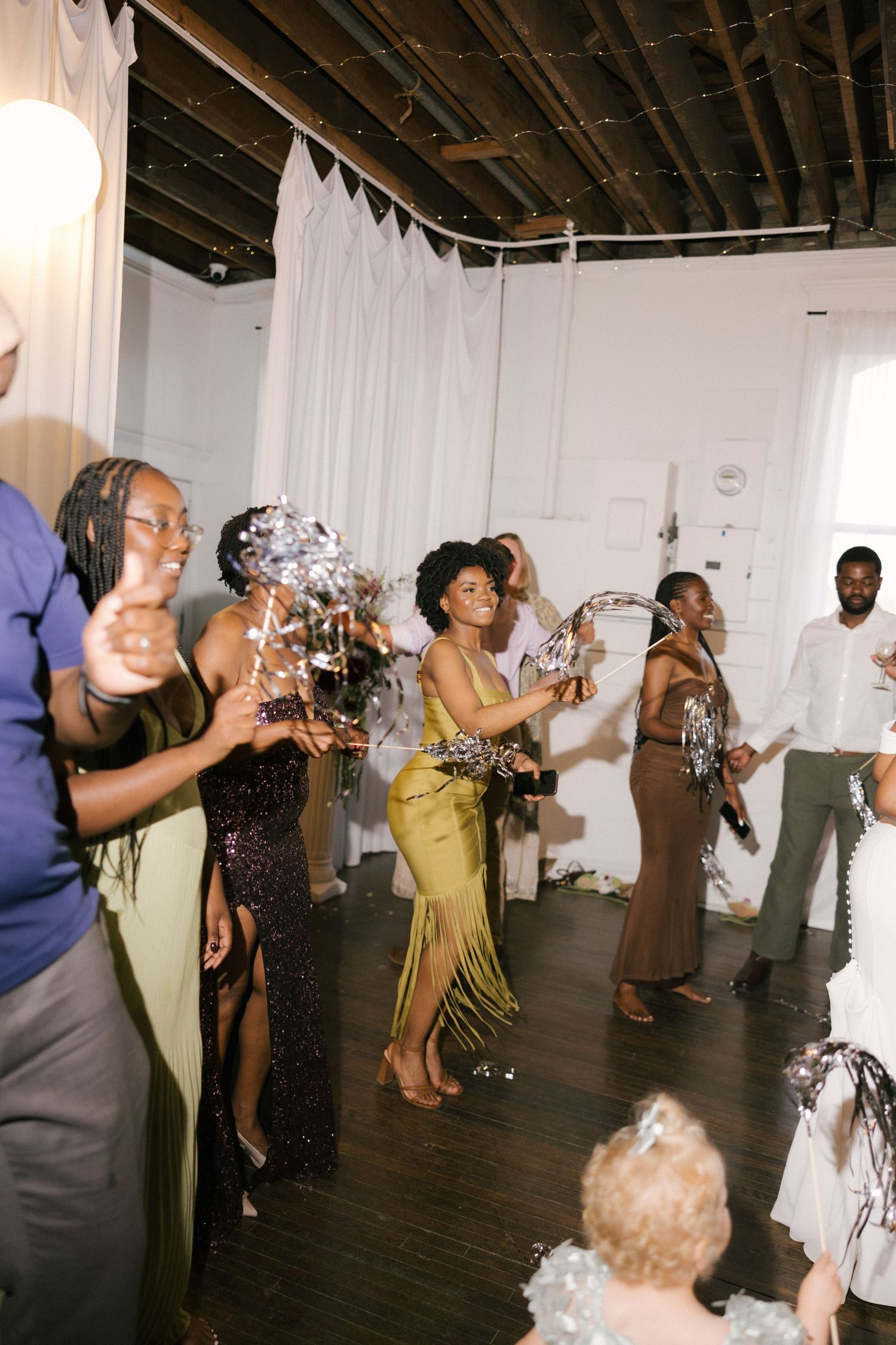 Guests in elegant attire dancing and celebrating at an indoor party with confetti and decorations.