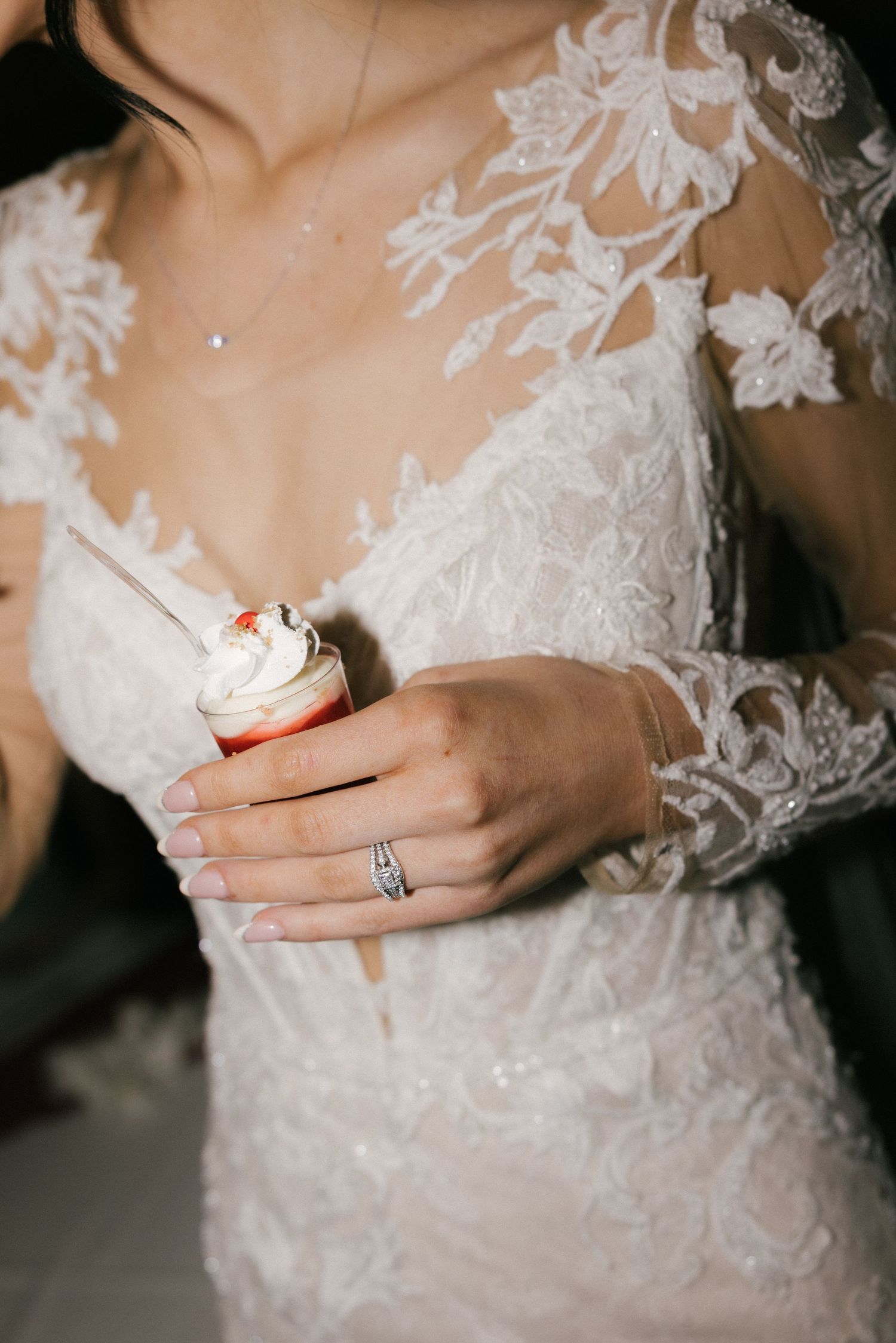 Close-up details of a bride's lace wedding dress and engagement ring against a neutral background.