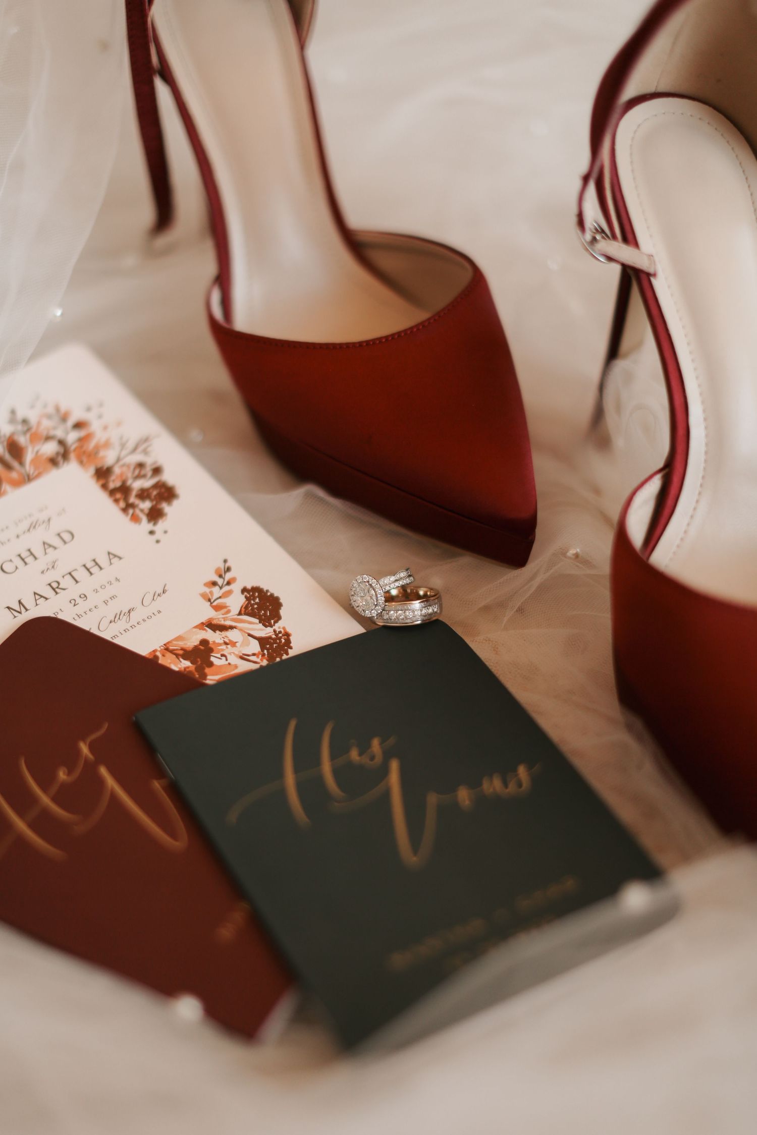 Wedding details flat lay with burgundy heels, vow books, and engagement ring.