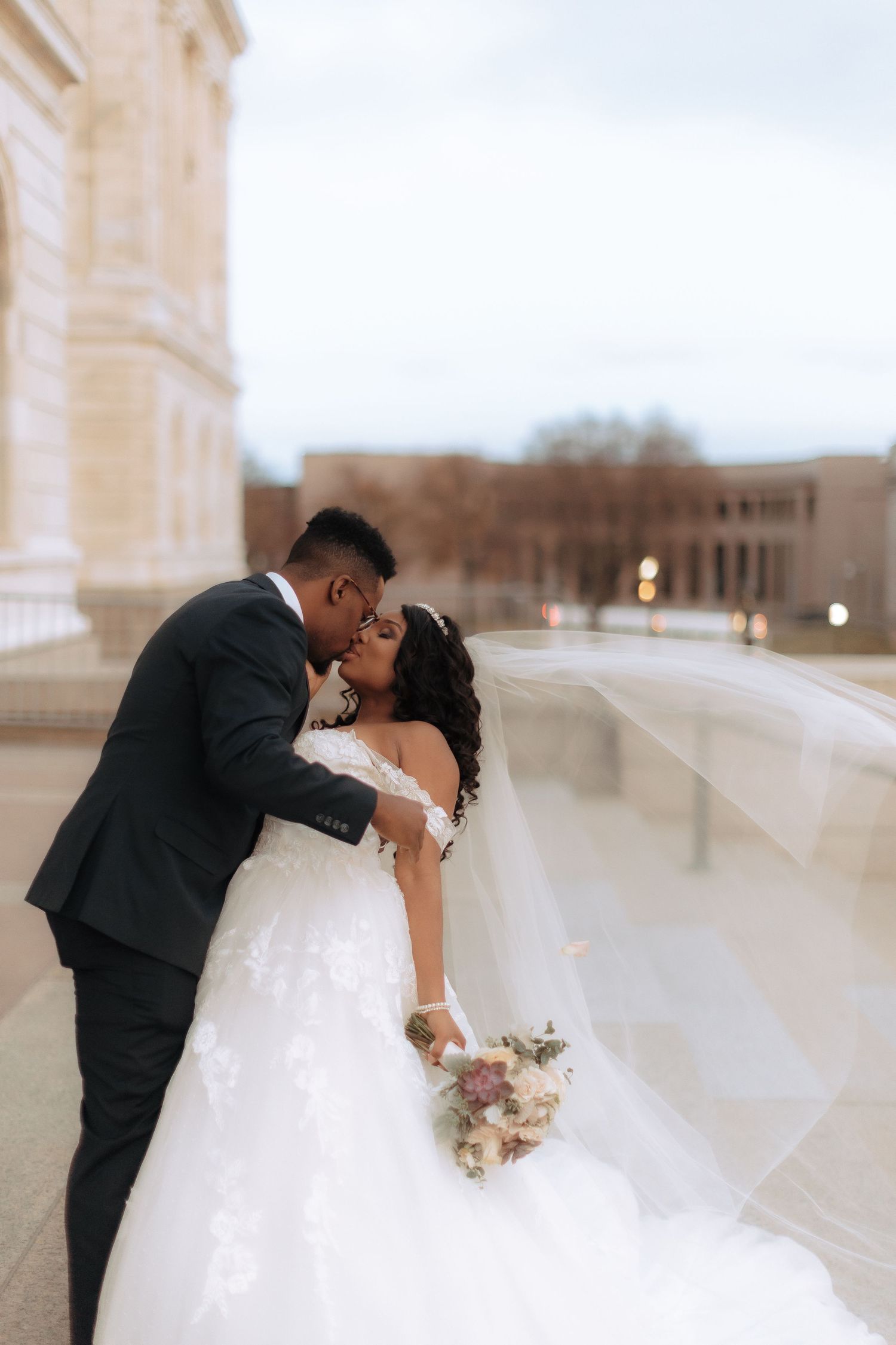 A romantic wedding couple sharing a kiss on an elegant outdoor balcony.